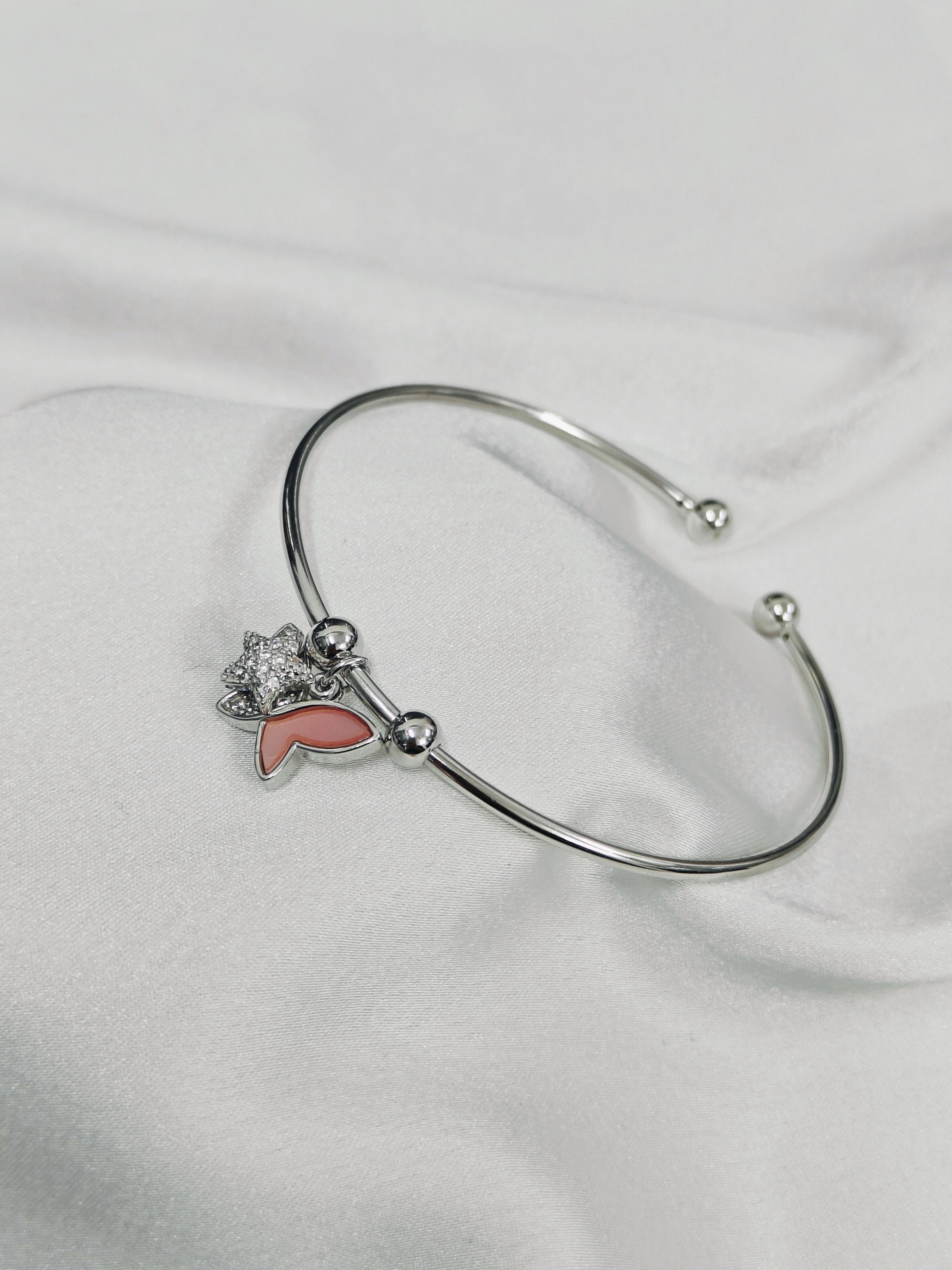 Silver bracelet with a pink heart charm on a white fabric background