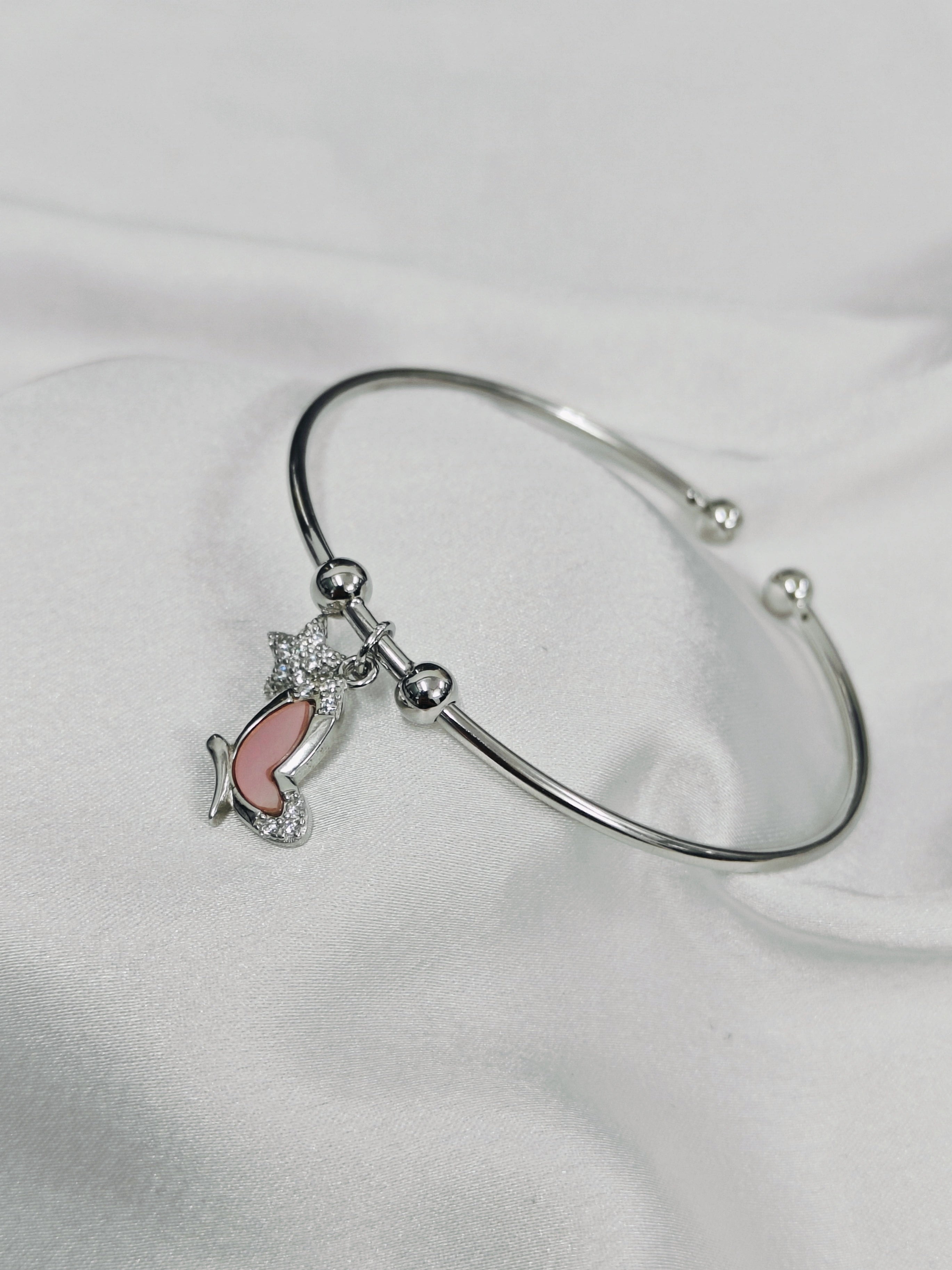 Silver bracelet with a pink fish charm on a white background