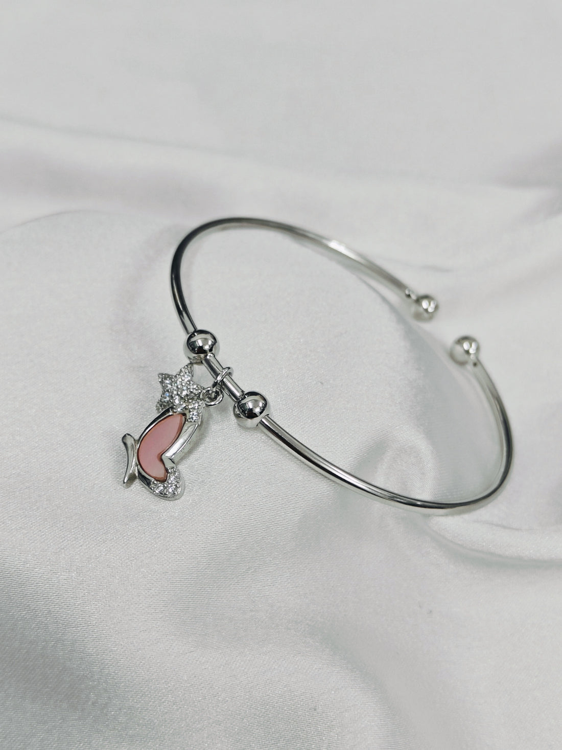 Silver bracelet with a pink fish charm on a white background