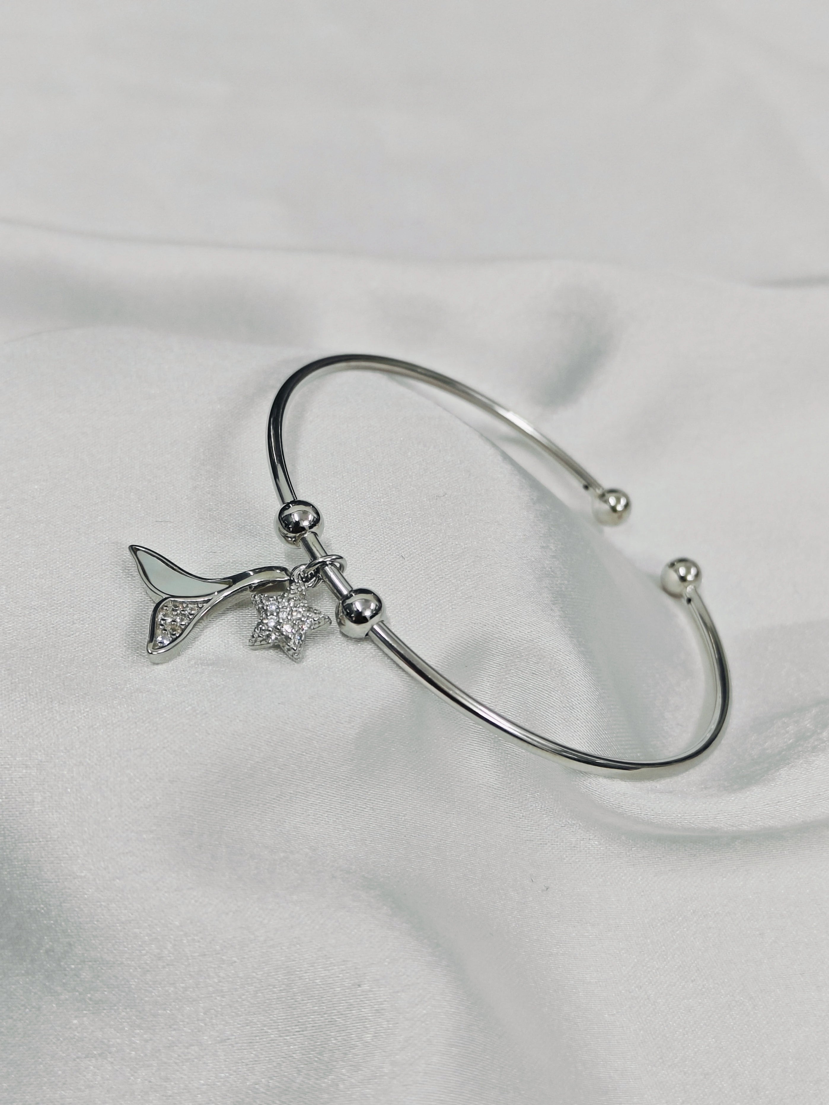 Silver bracelet with a star and leaf charm on a light gray background
