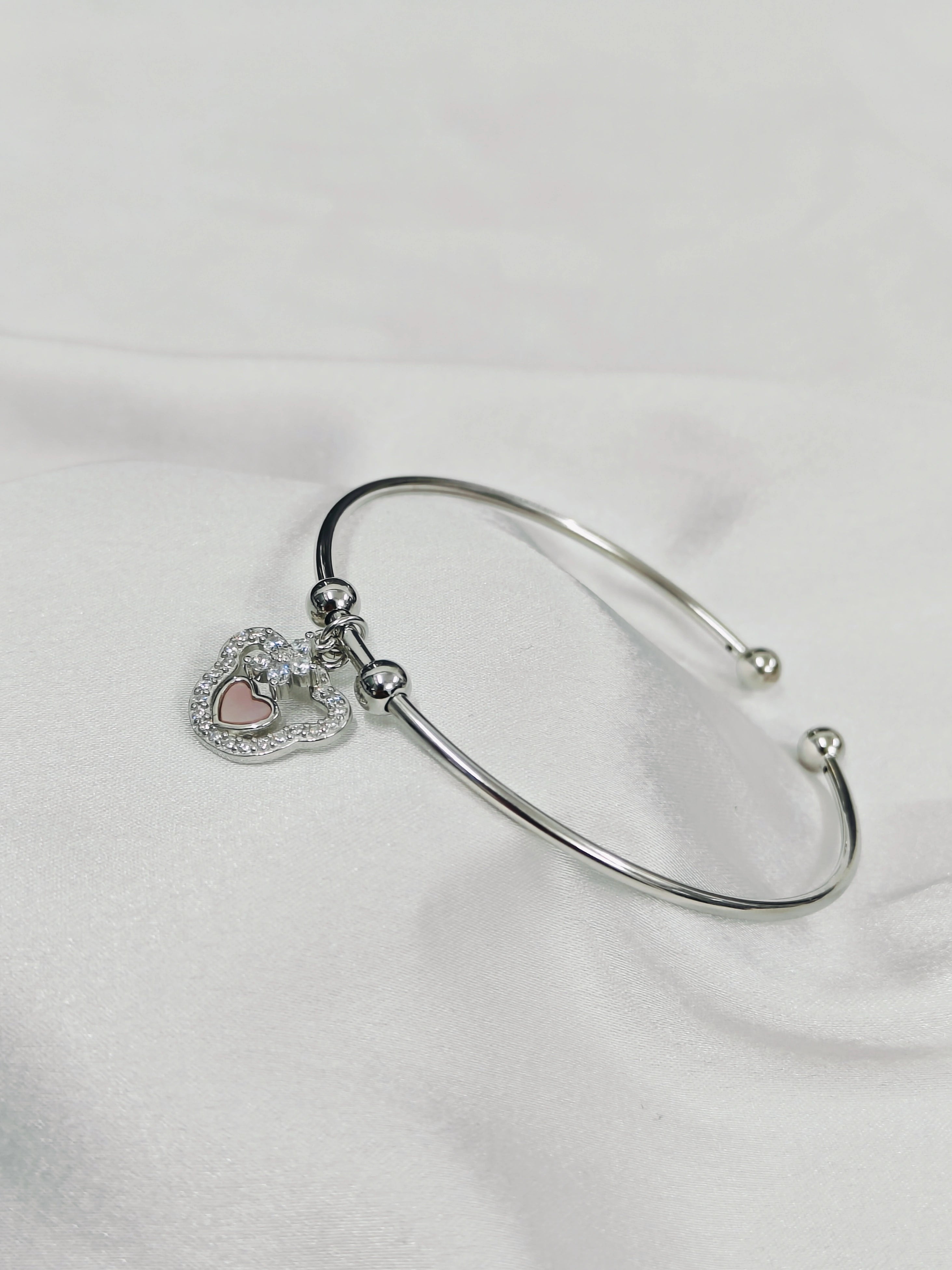 Silver bangle with a heart-shaped charm on a white background