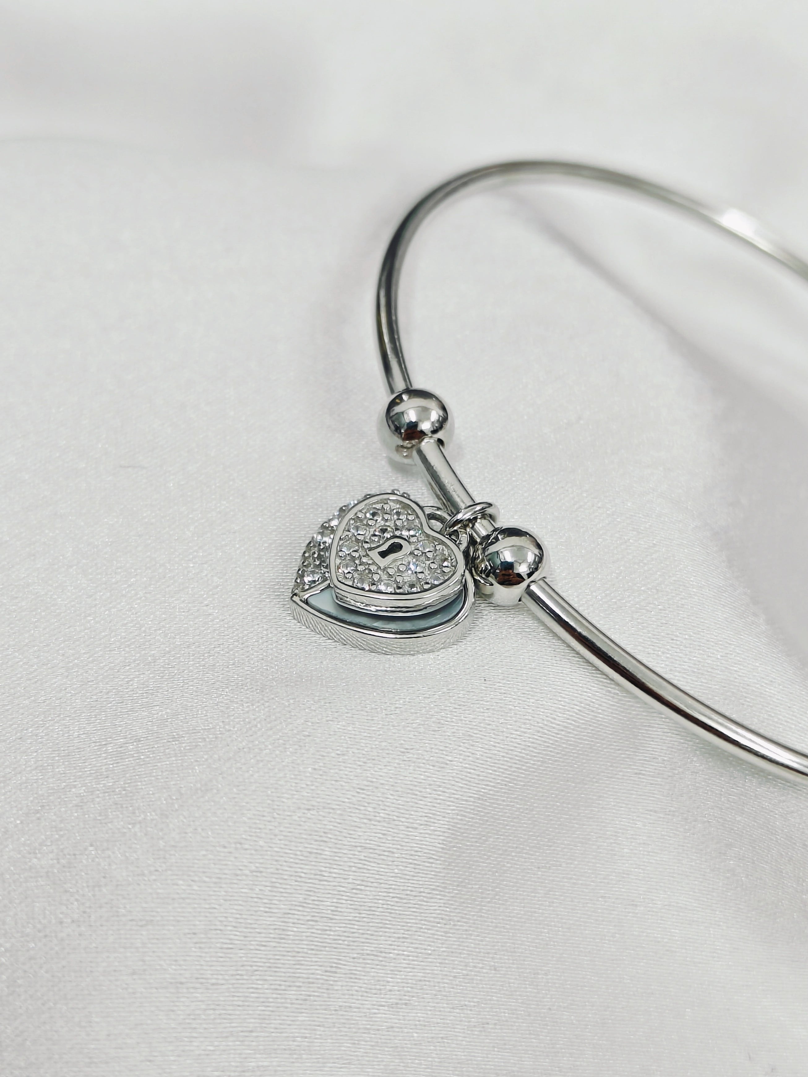 Silver bangle with a heart-shaped lock charm on a white background