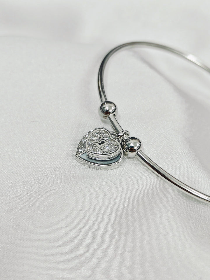 Silver bangle with a heart-shaped lock charm on a white background