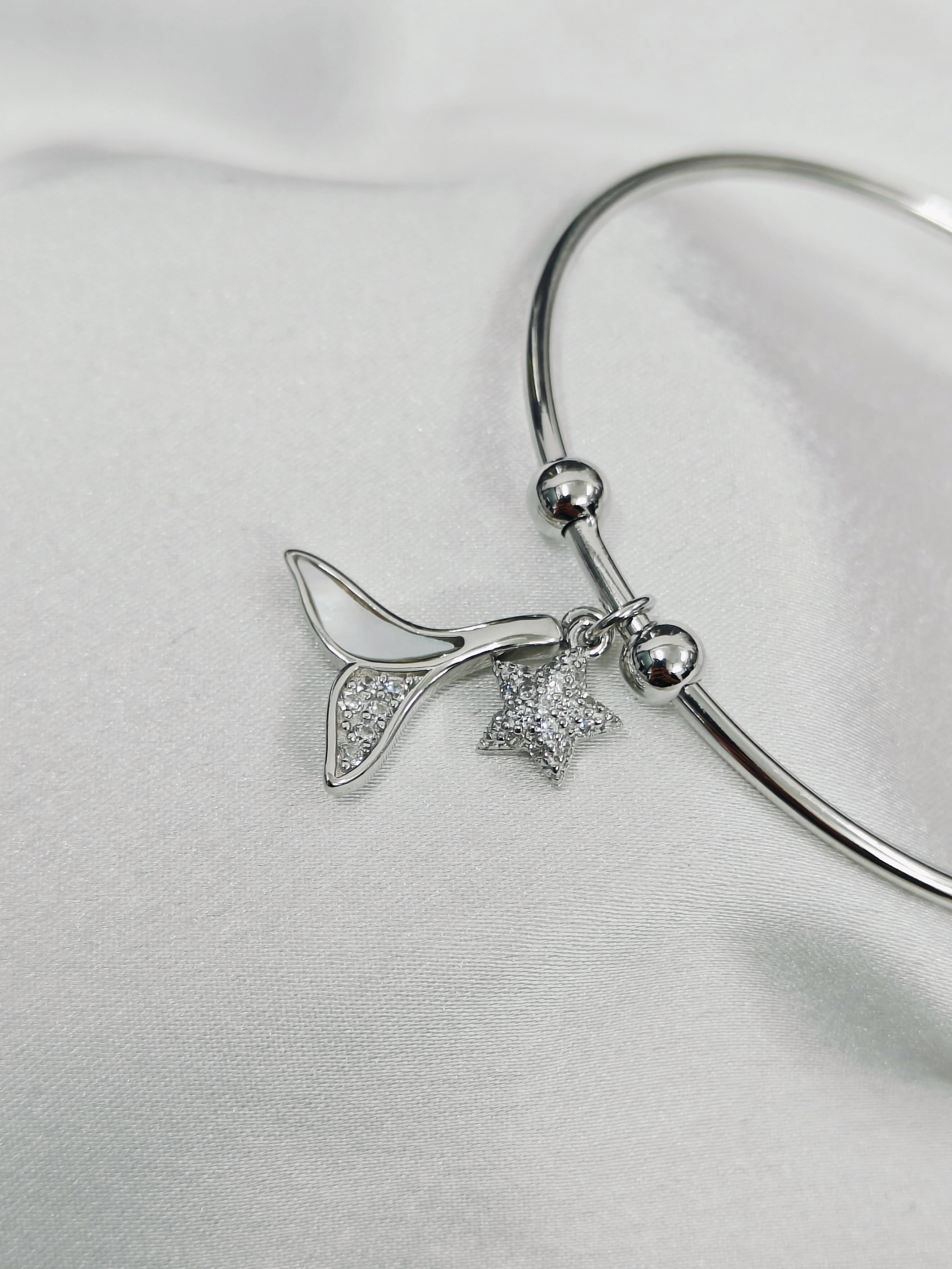 Silver bracelet with star and leaf charms on a light gray background