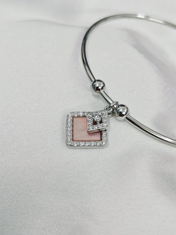 Silver bracelet with a square charm featuring pink and white design on a light gray background