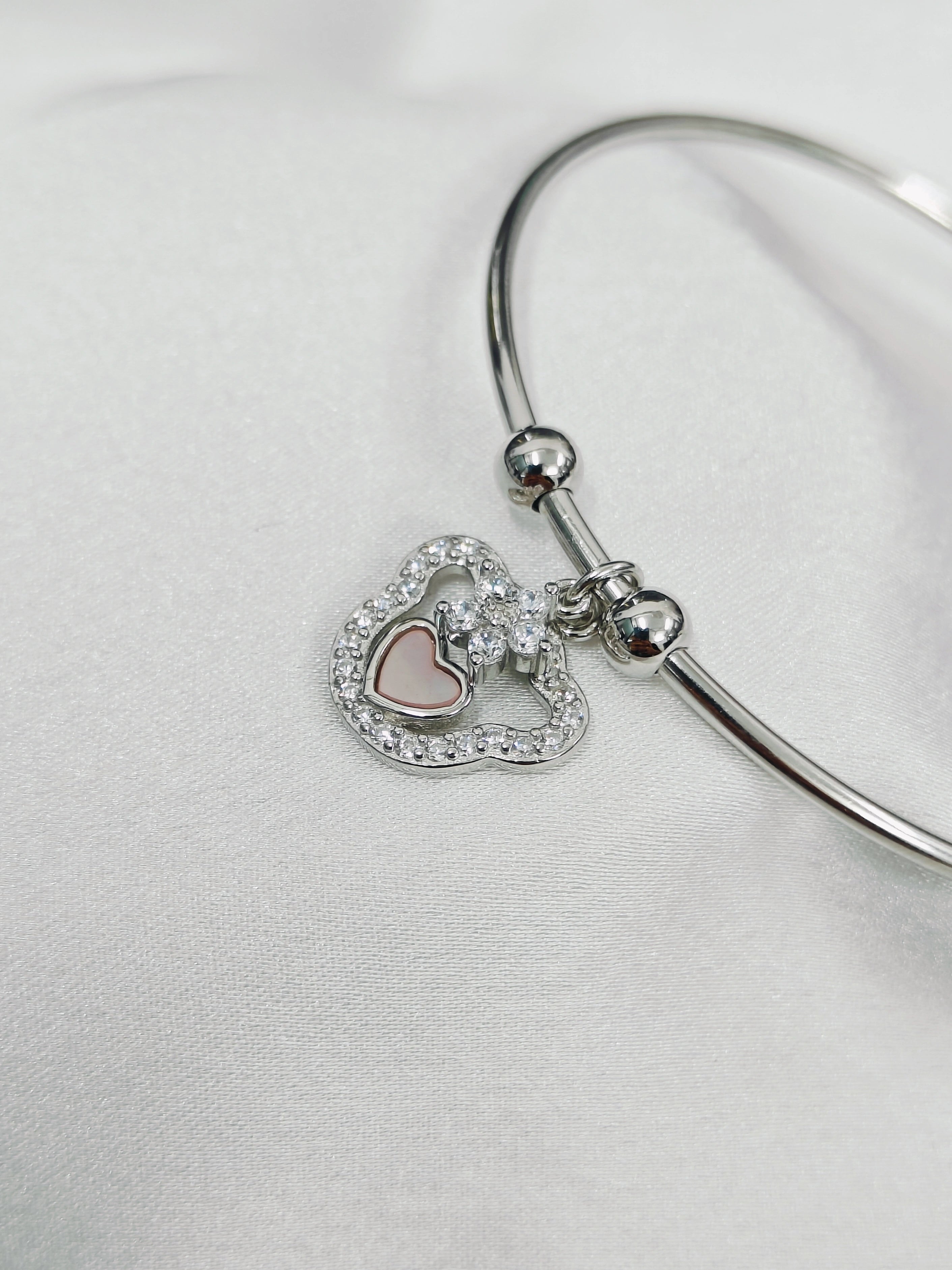 Silver bangle with heart-shaped charms on a light gray background