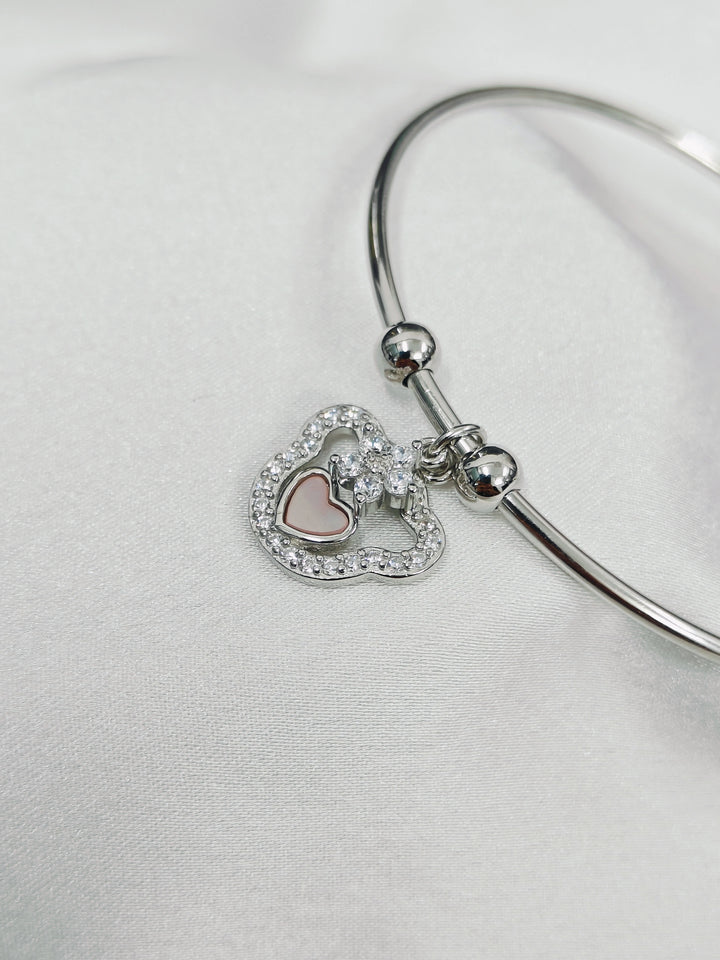Silver bangle with heart-shaped charms on a light gray background