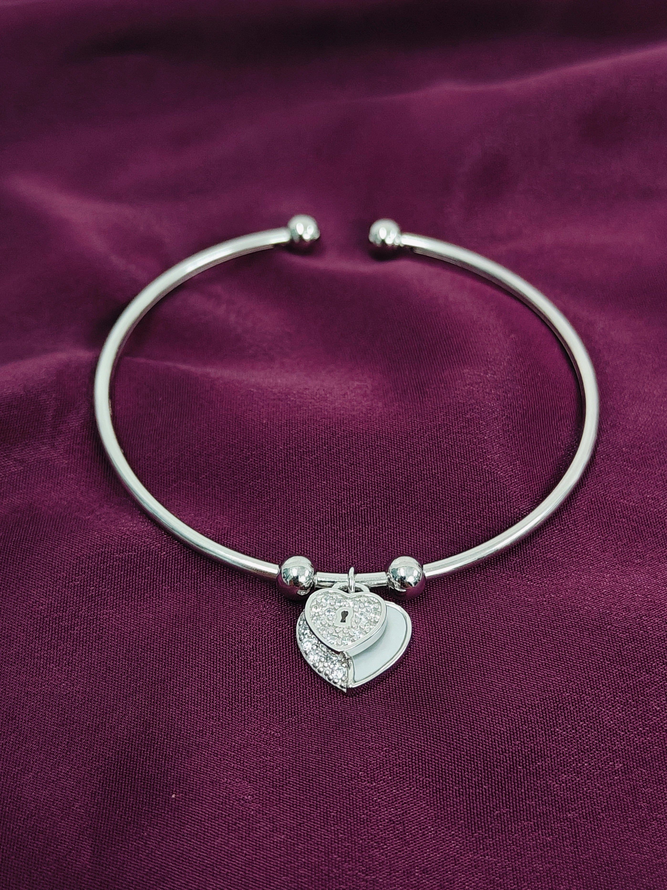 Silver bracelet with a heart-shaped charm on a purple fabric background