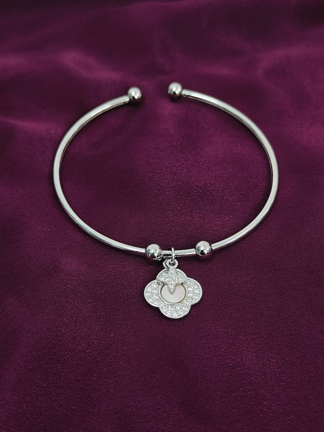 Silver bracelet with a heart charm on a purple fabric background