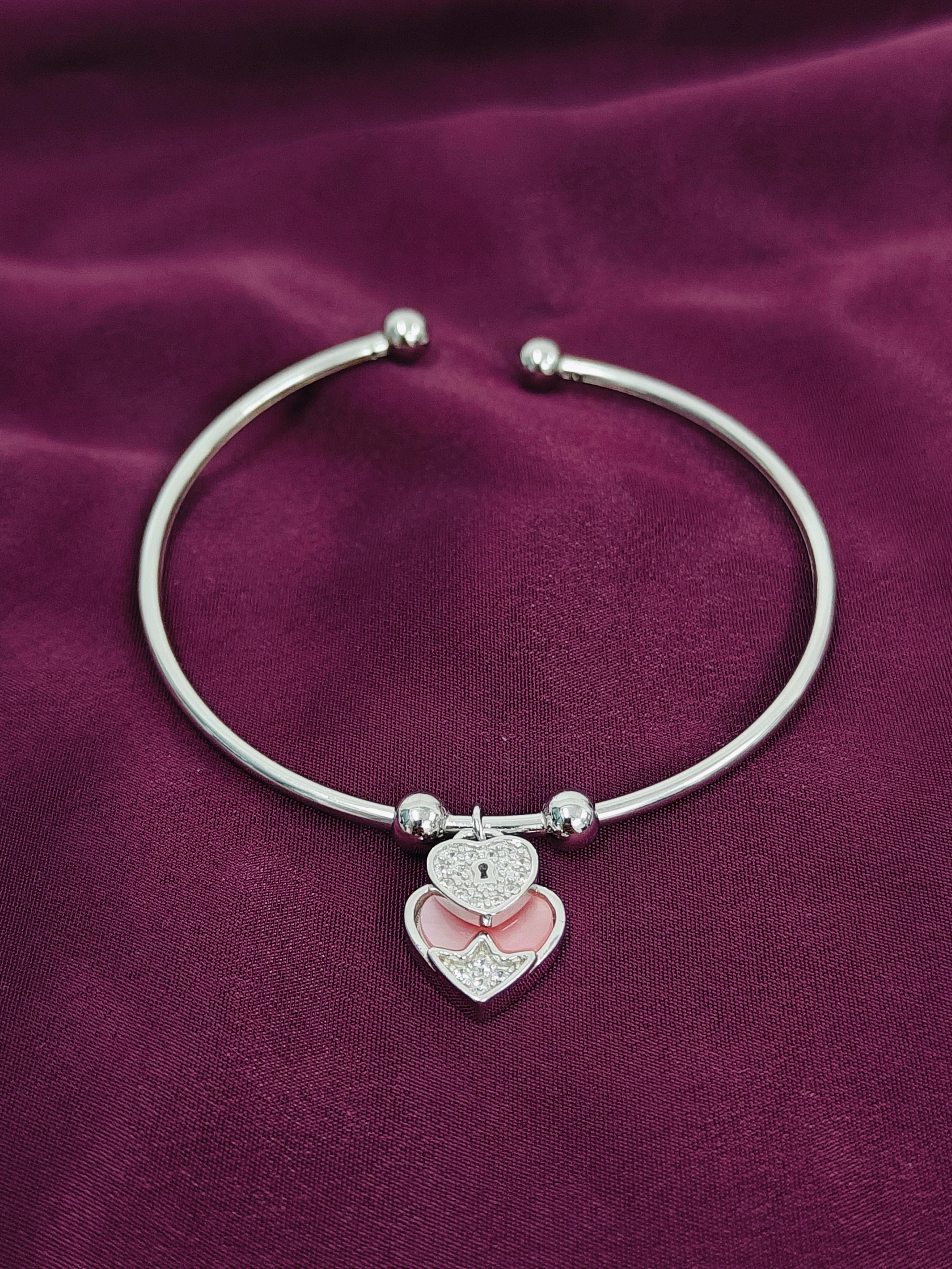 Silver bracelet with a heart-shaped charm on a purple fabric background