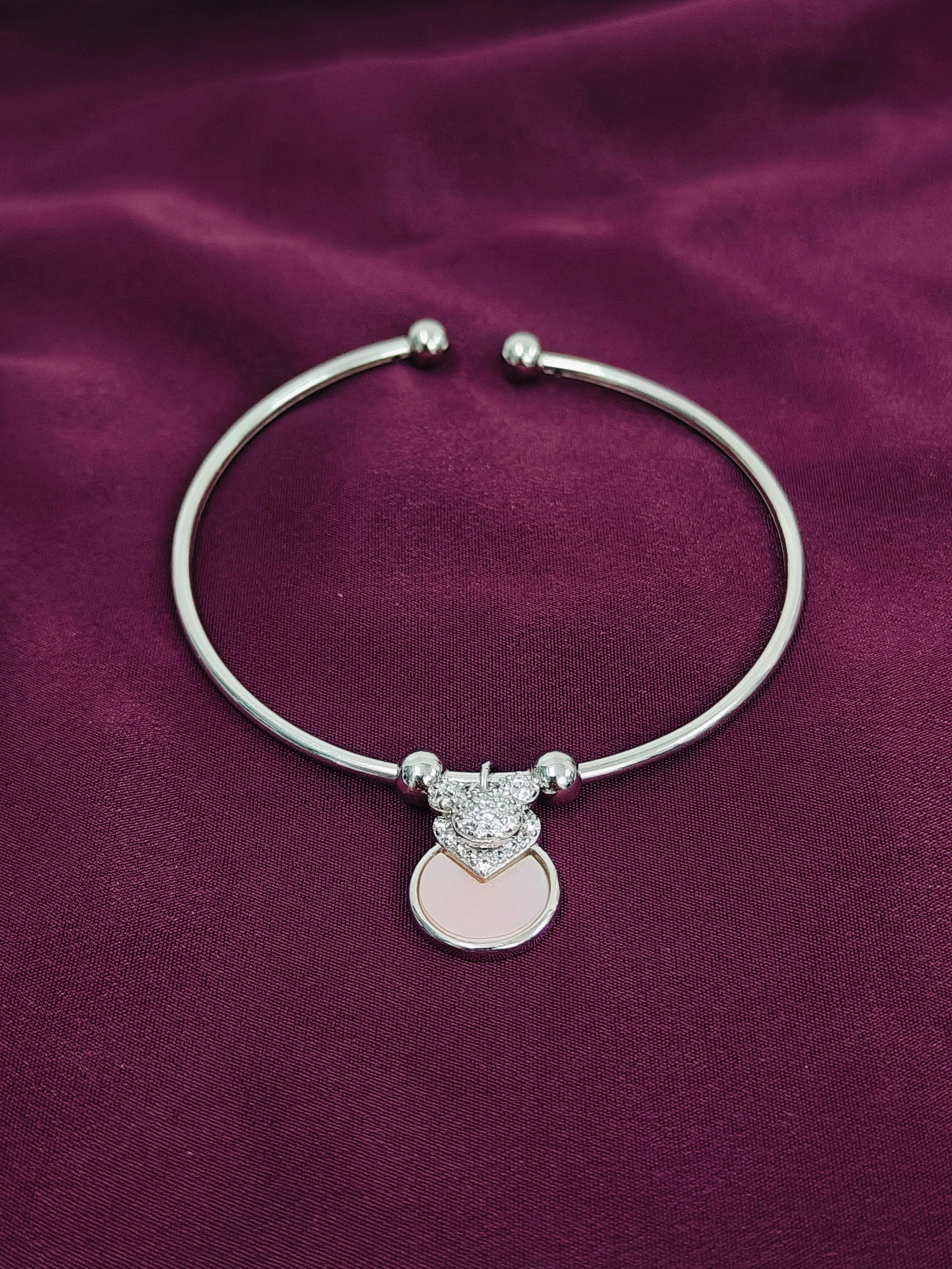 Silver bracelet with a heart-shaped charm on a purple fabric background