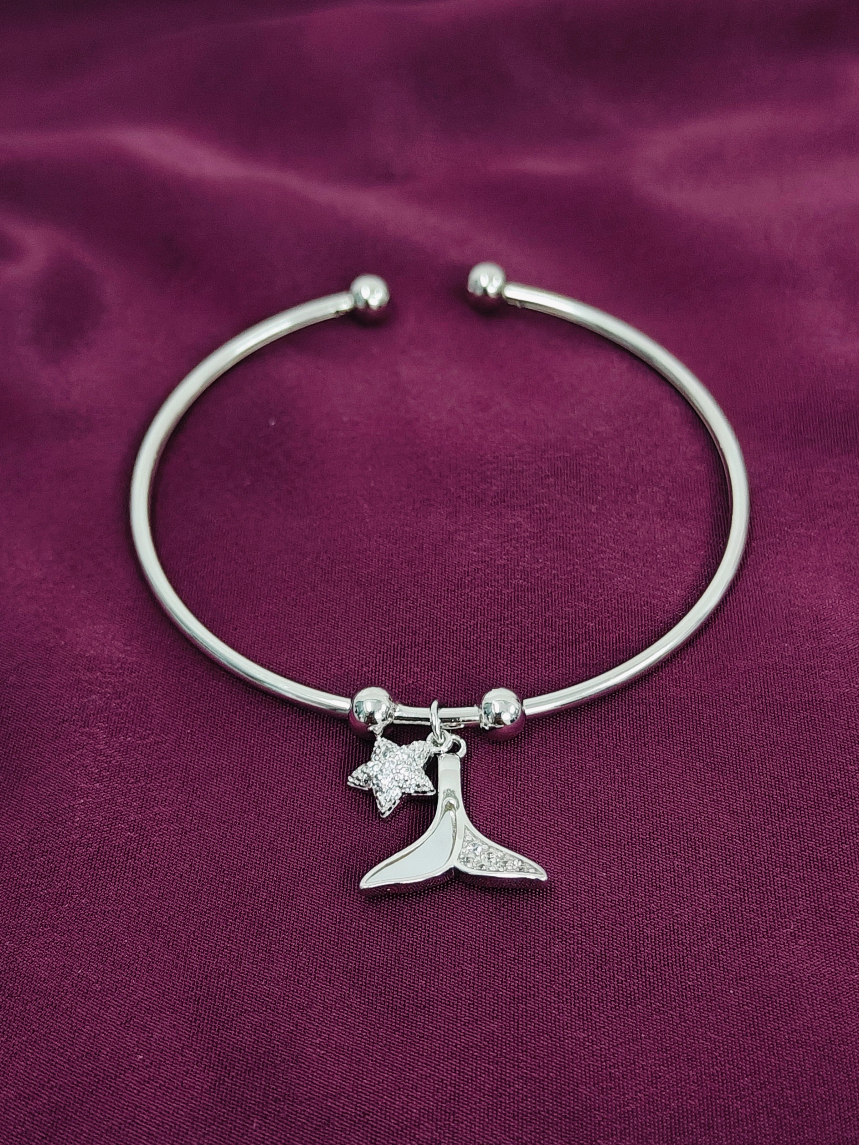 Silver bracelet with a whale tail and star charm on a purple fabric background
