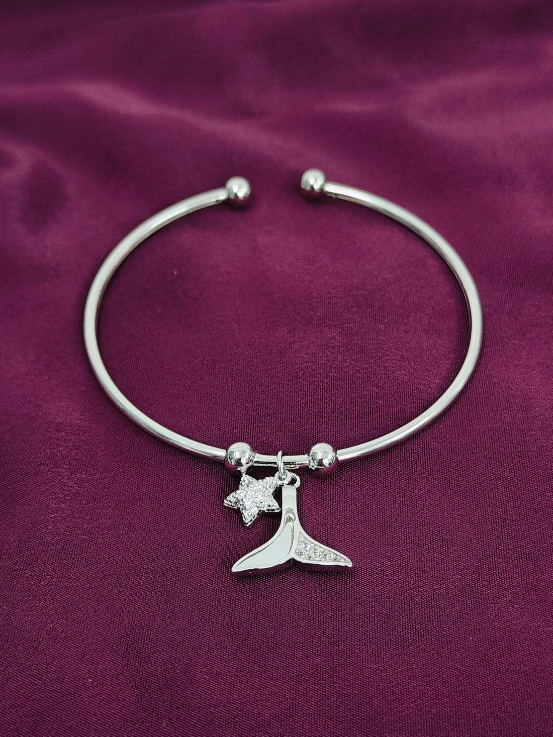 Silver bracelet with a whale tail and star charm on a purple fabric background