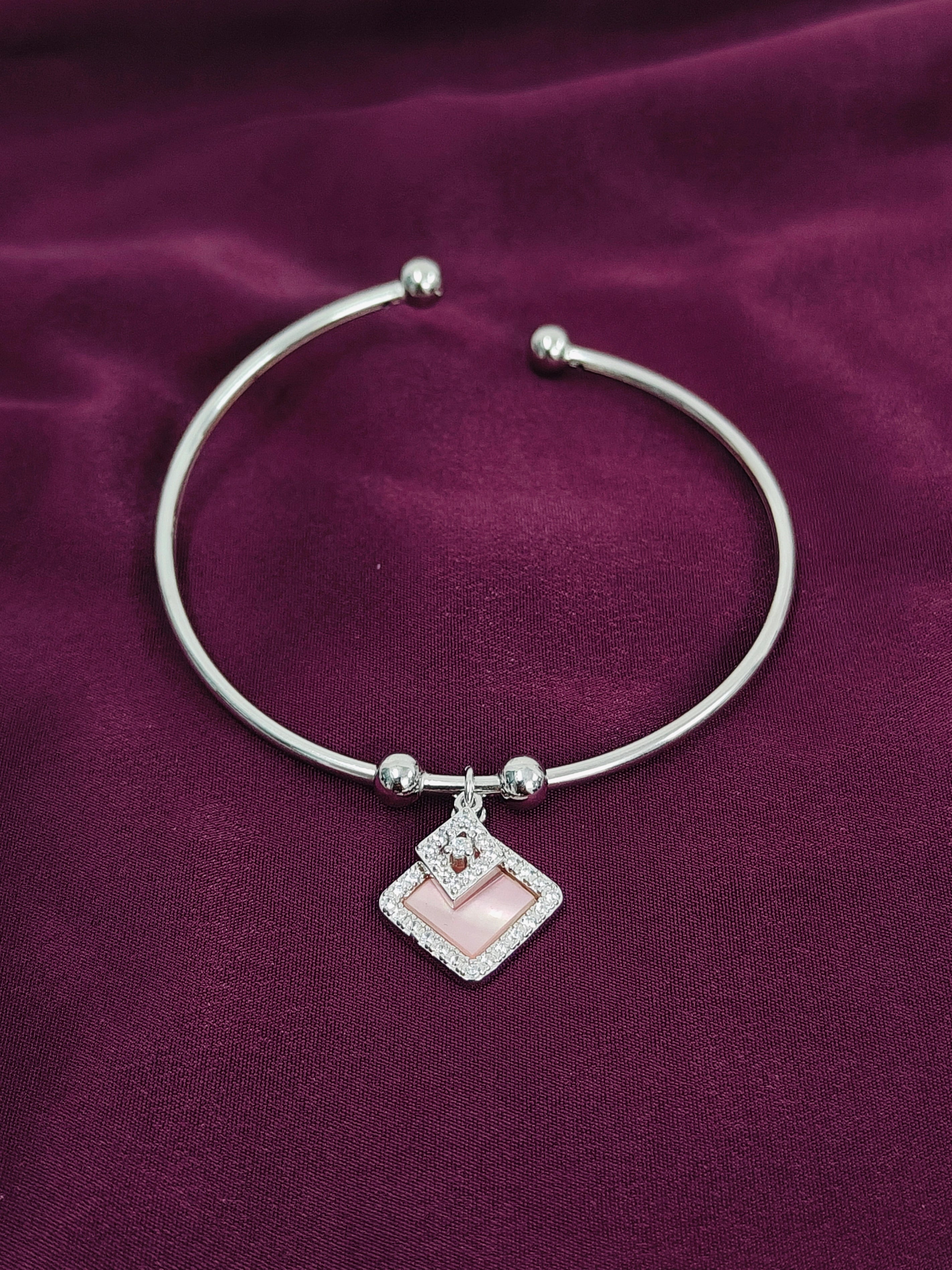 Silver bracelet with a pink charm on a purple fabric background