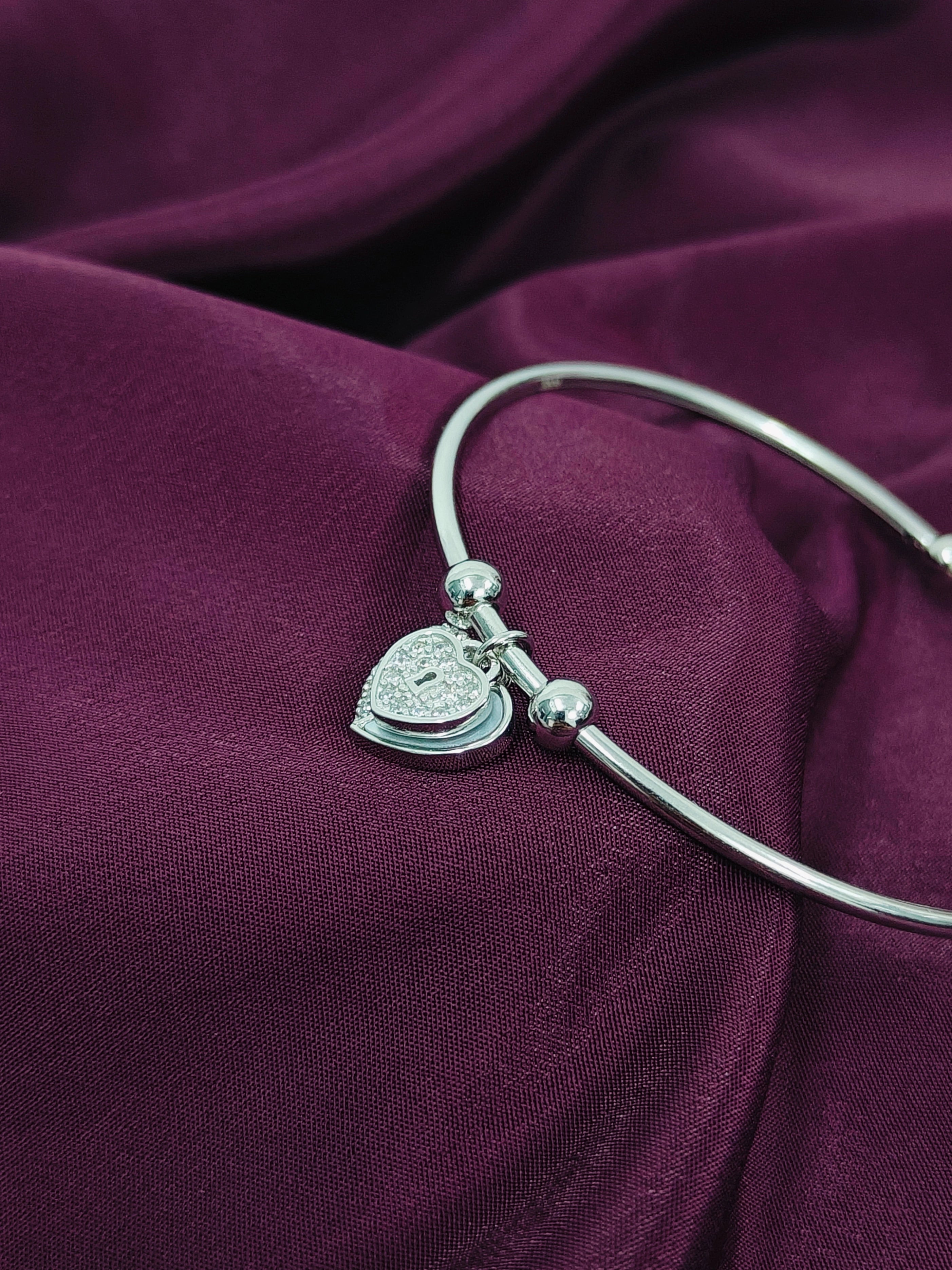 Silver bracelet with a heart-shaped charm on a purple fabric background