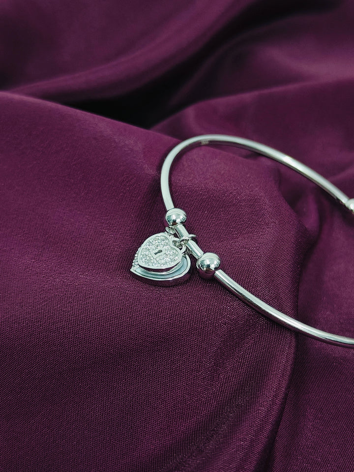 Silver bracelet with a heart-shaped charm on a purple fabric background