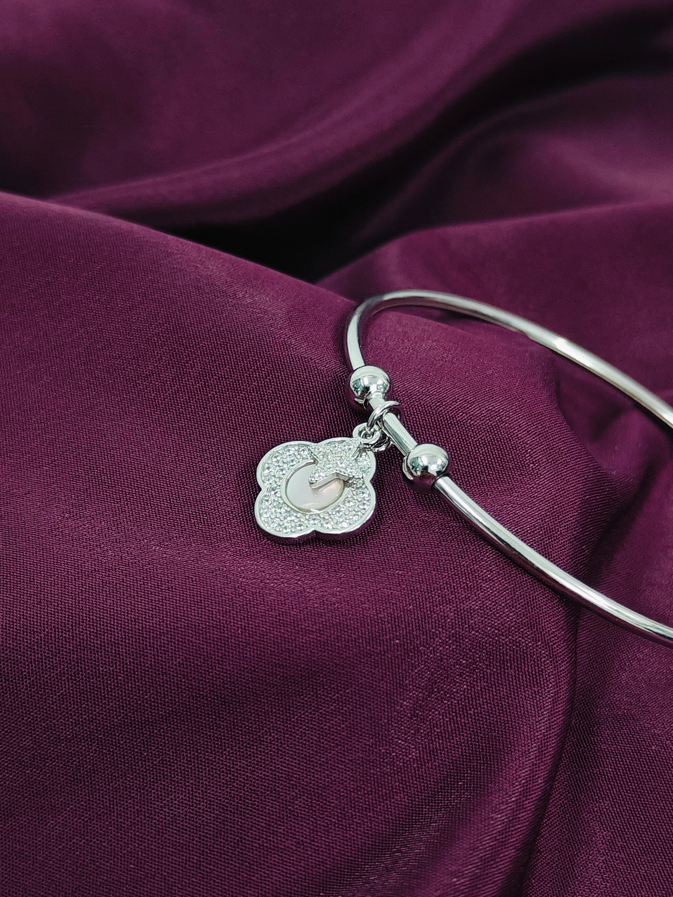 Silver bangle with a decorative charm on a purple fabric background