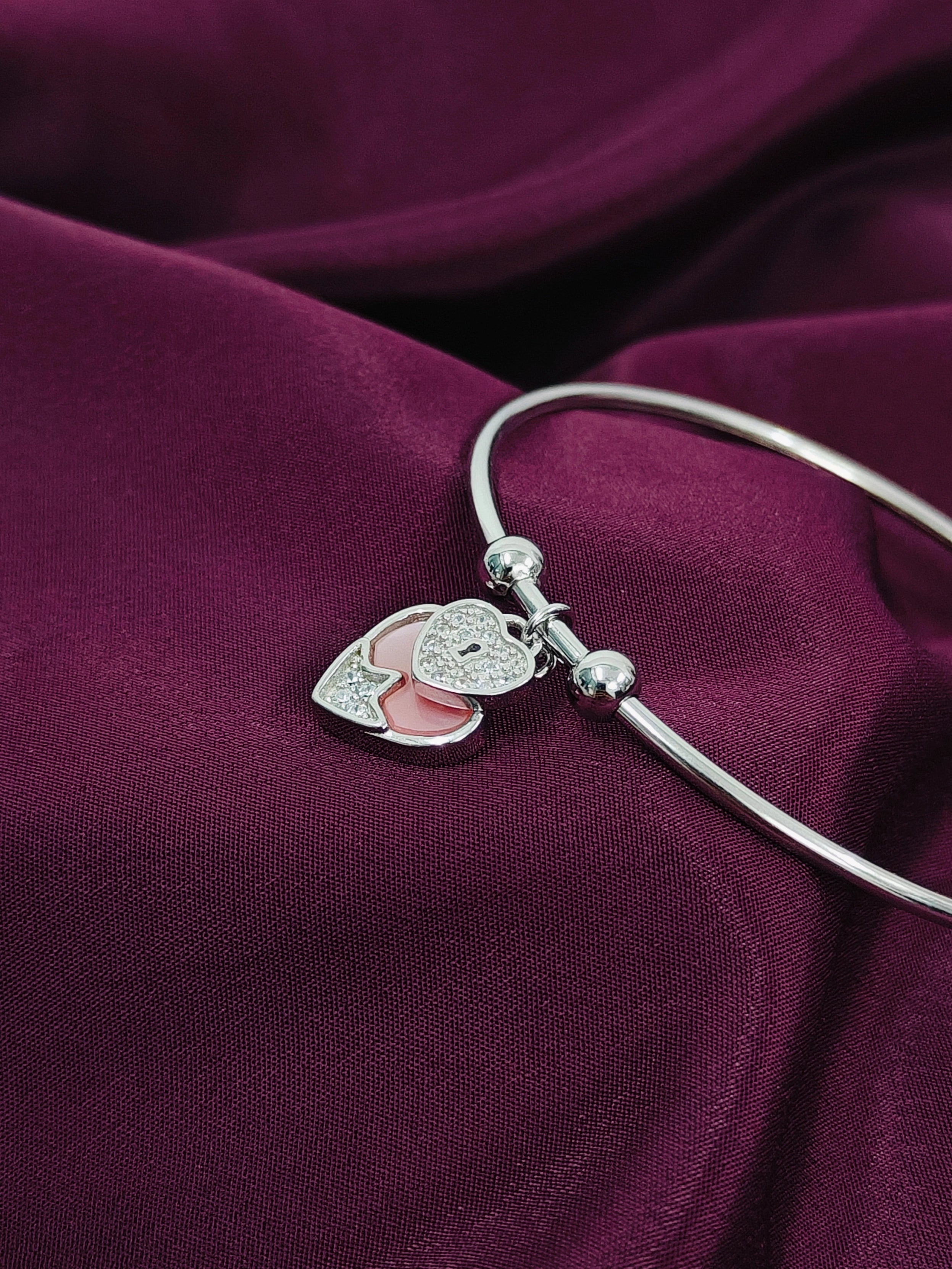 Silver bracelet with heart-shaped charm on a purple fabric background