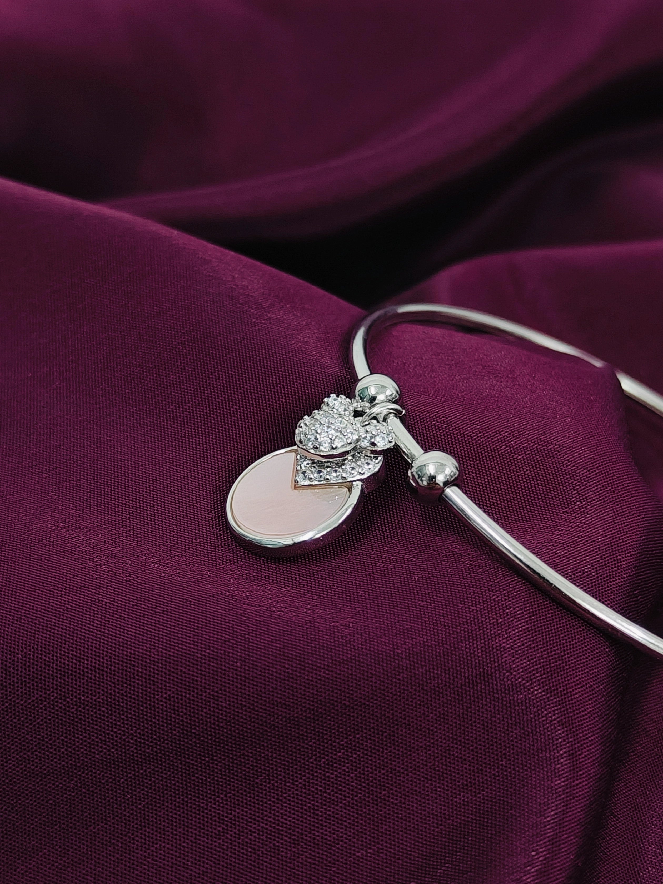 Silver bracelet with heart-shaped charm on a purple fabric background