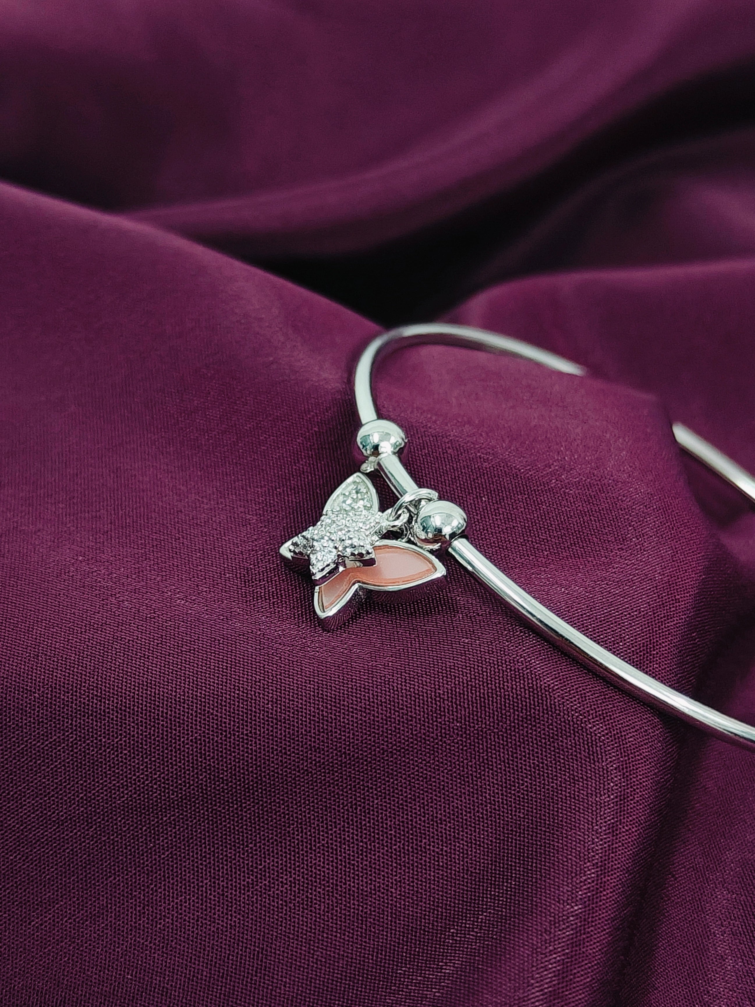 Silver bracelet with a butterfly charm on a purple fabric background