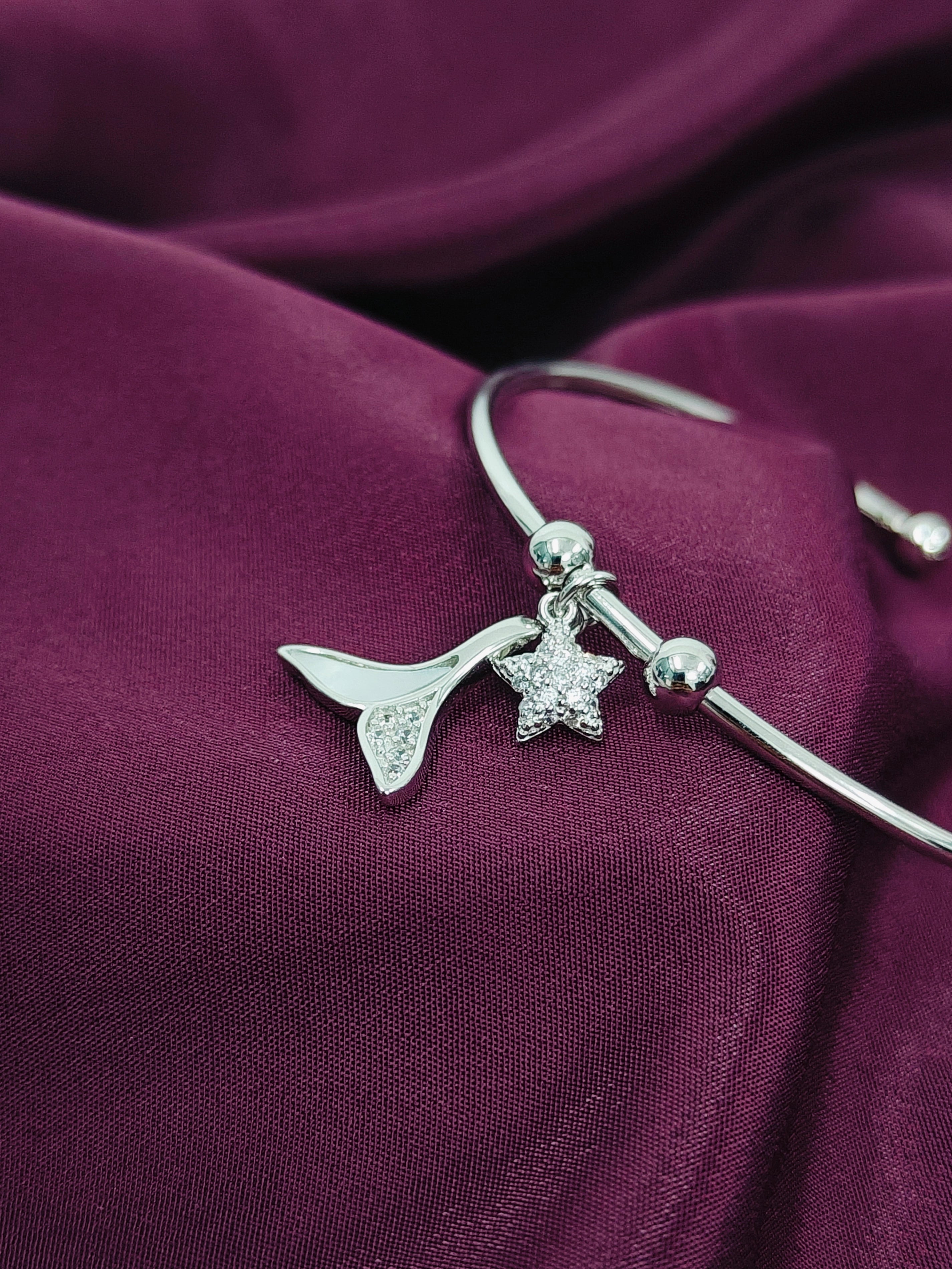 Silver bracelet with mermaid tail and starfish charm on a purple fabric background
