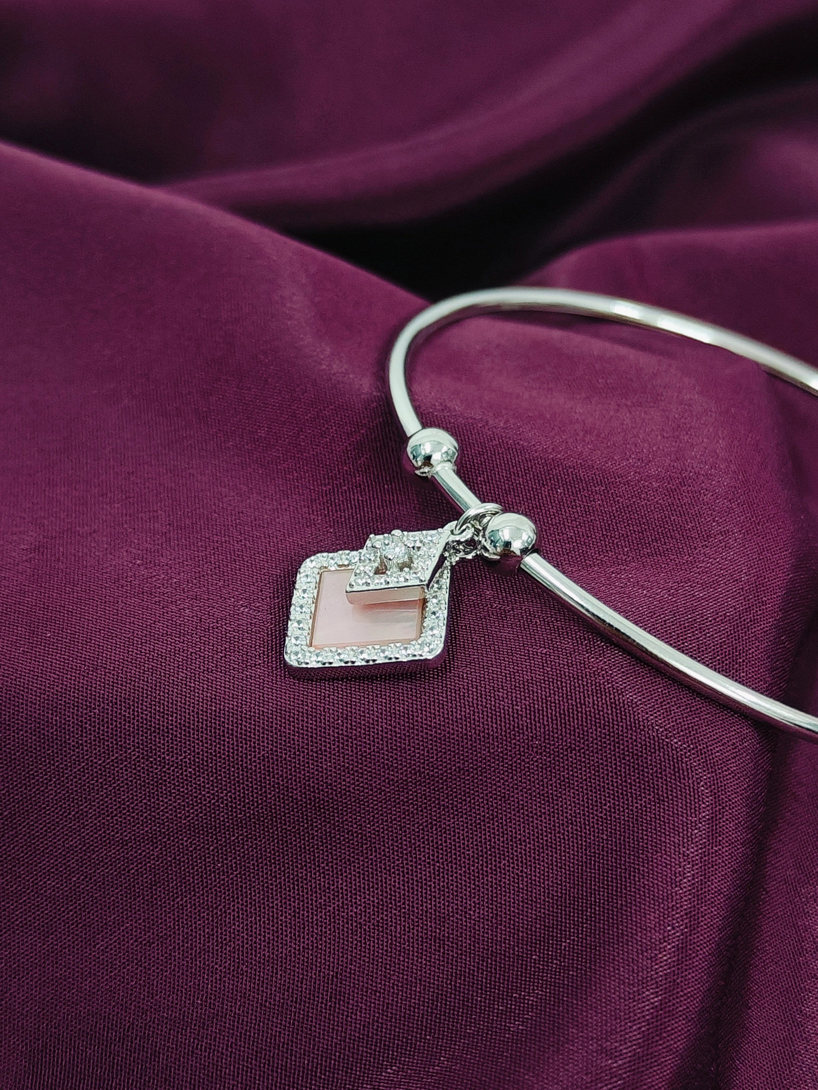 Silver bracelet with a square charm on a purple fabric background