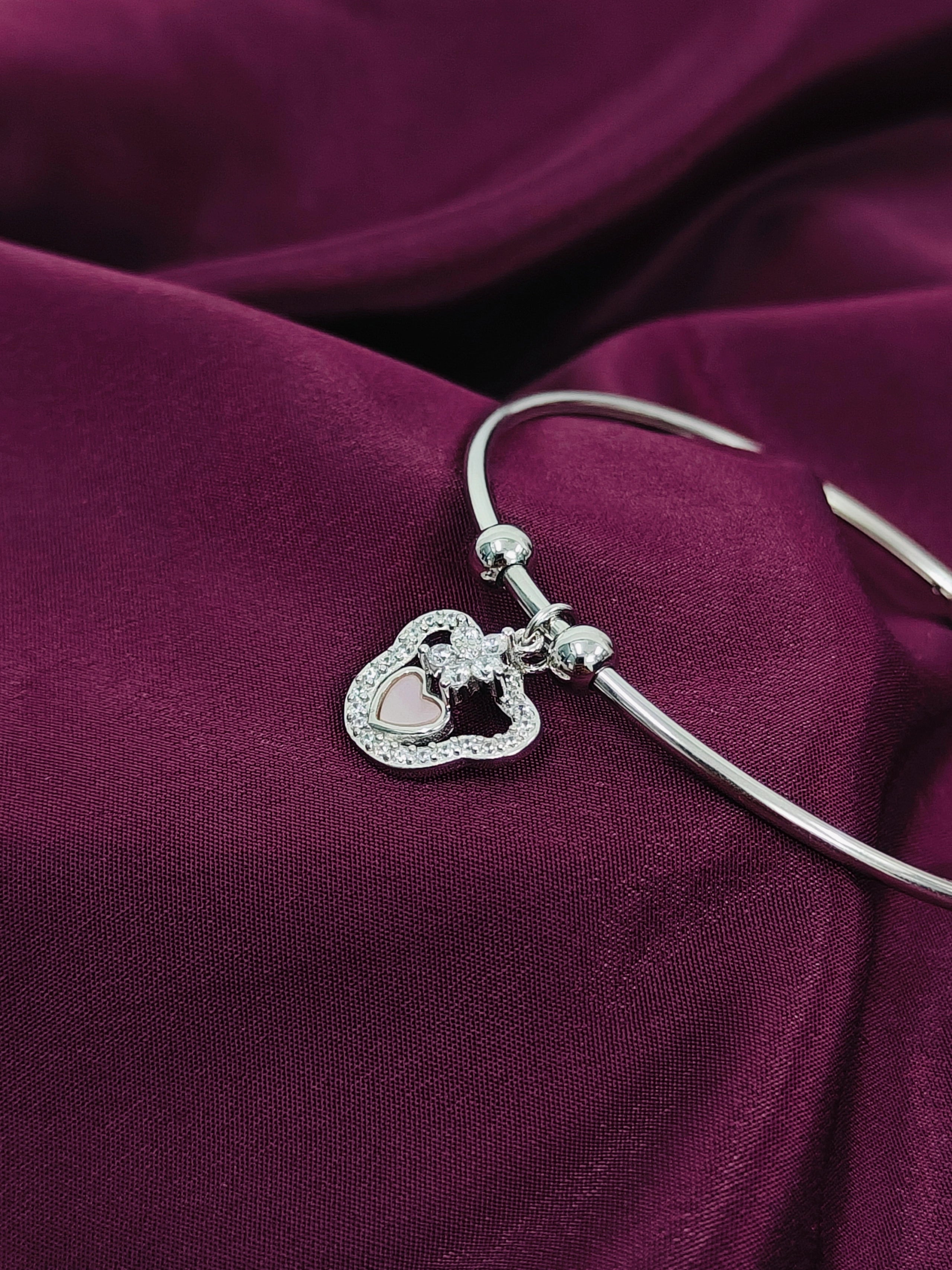 Silver bracelet with a heart-shaped charm on a purple fabric background