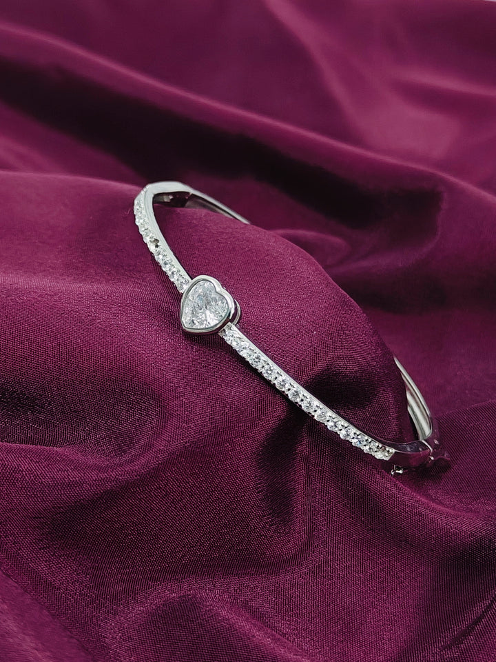 Silver bracelet with a heart-shaped diamond on a purple fabric background