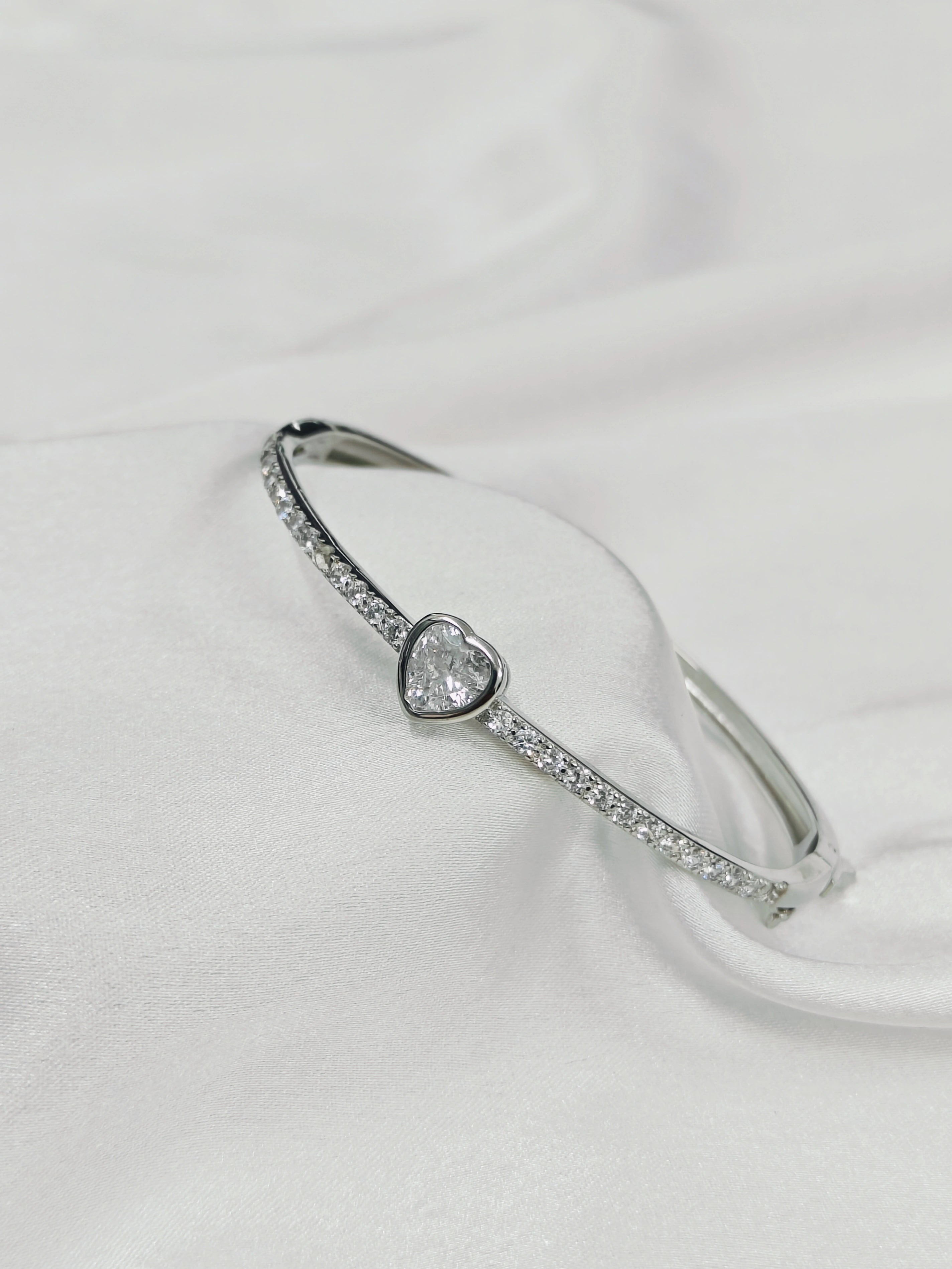 Silver bracelet with a heart-shaped diamond on a white background