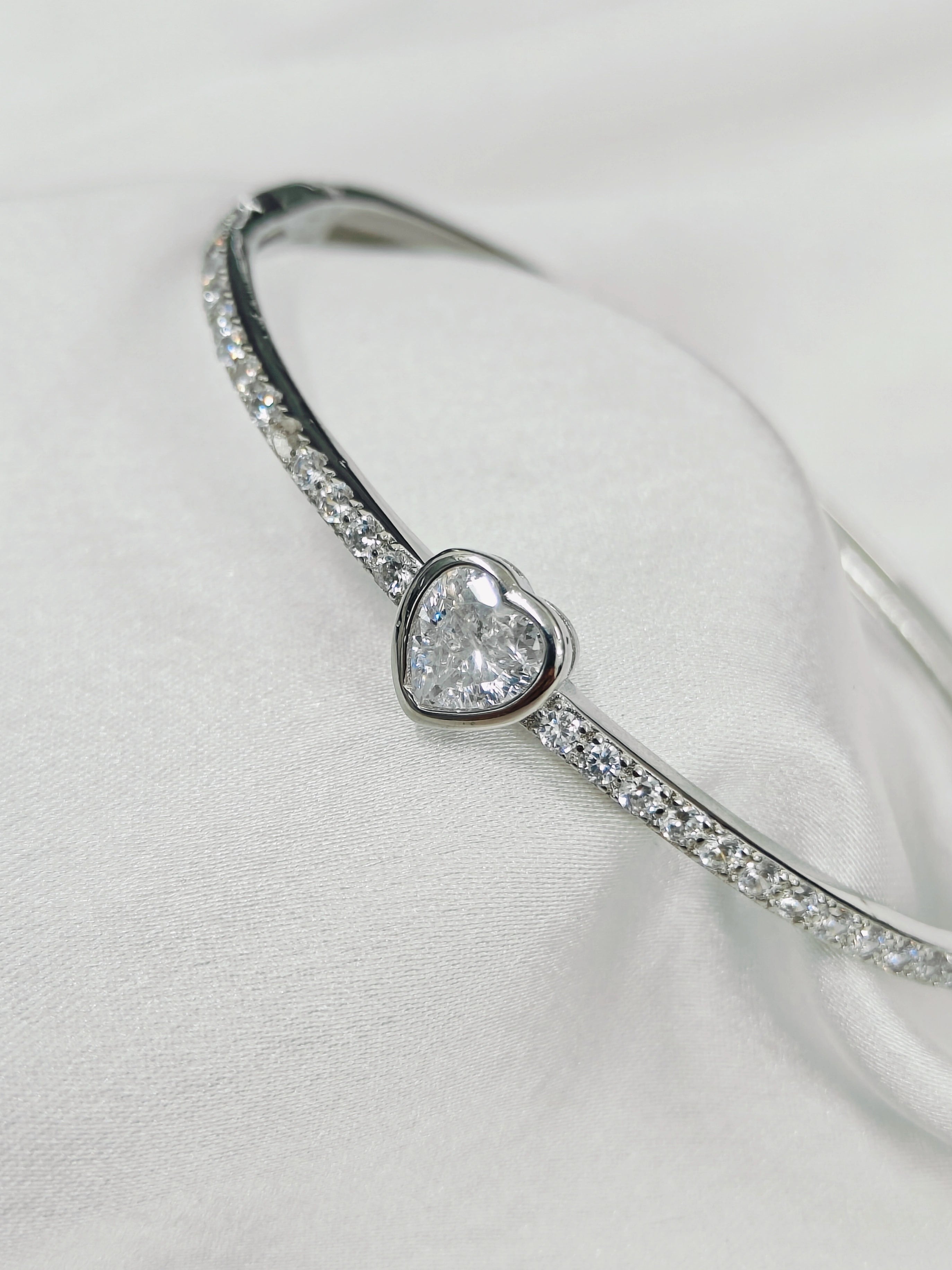 Silver bracelet with a heart-shaped diamond on a light gray background