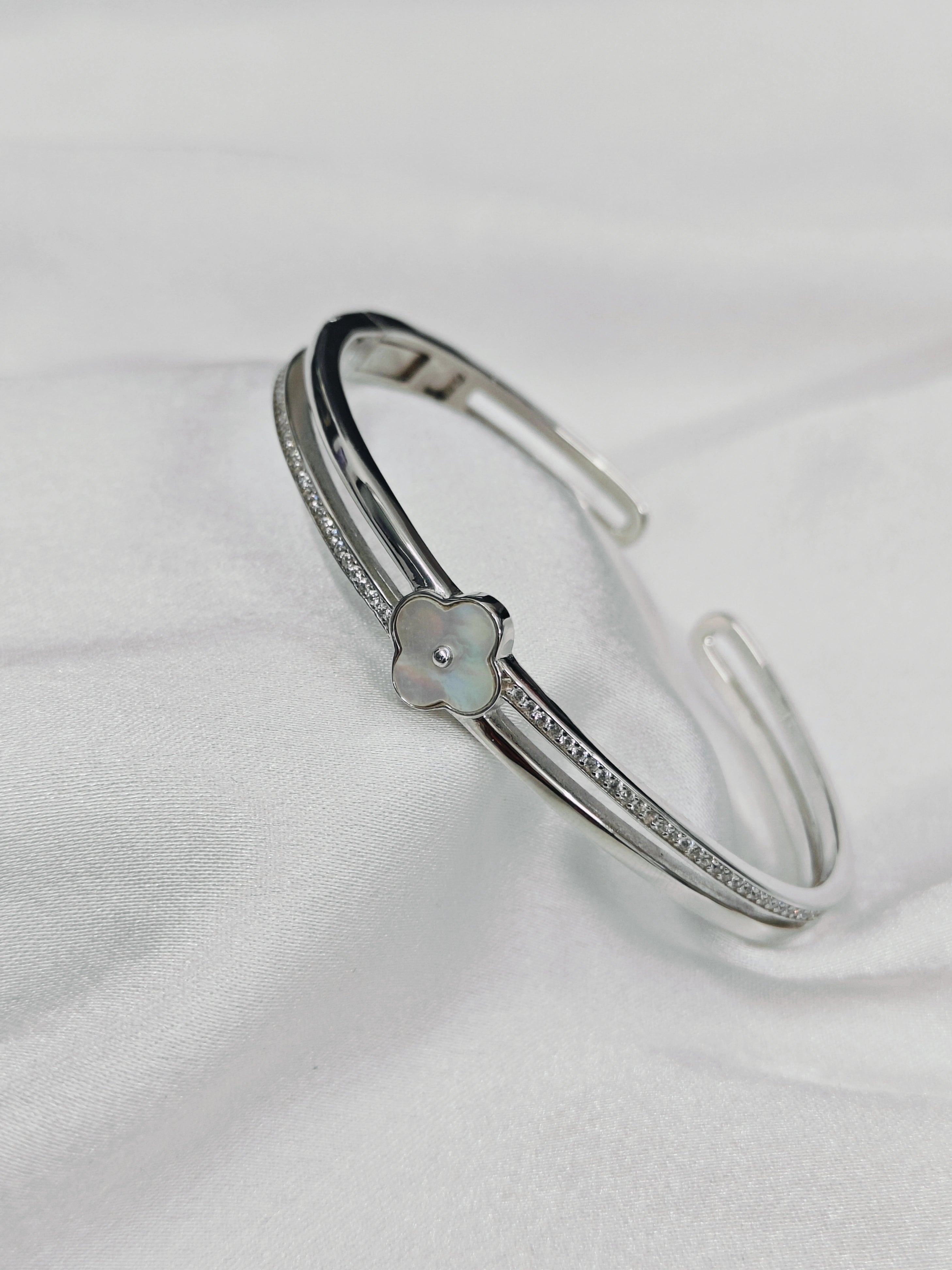 Silver bracelet with a clover charm on a white fabric background
