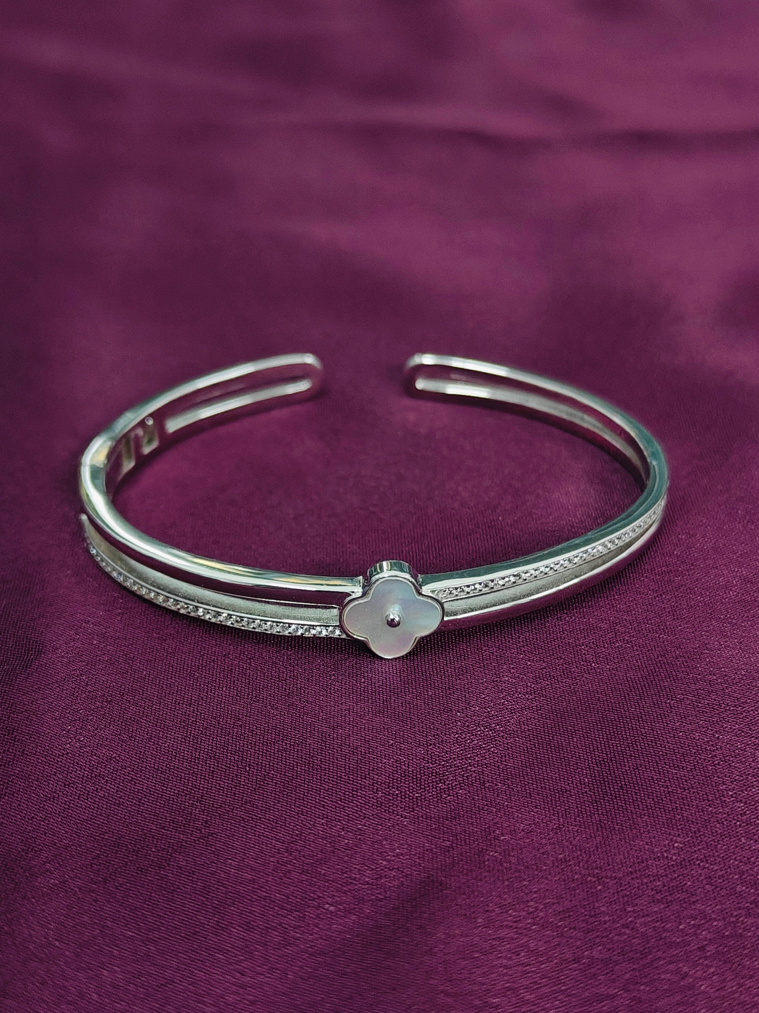 Silver bracelet with a clover charm on a purple fabric background