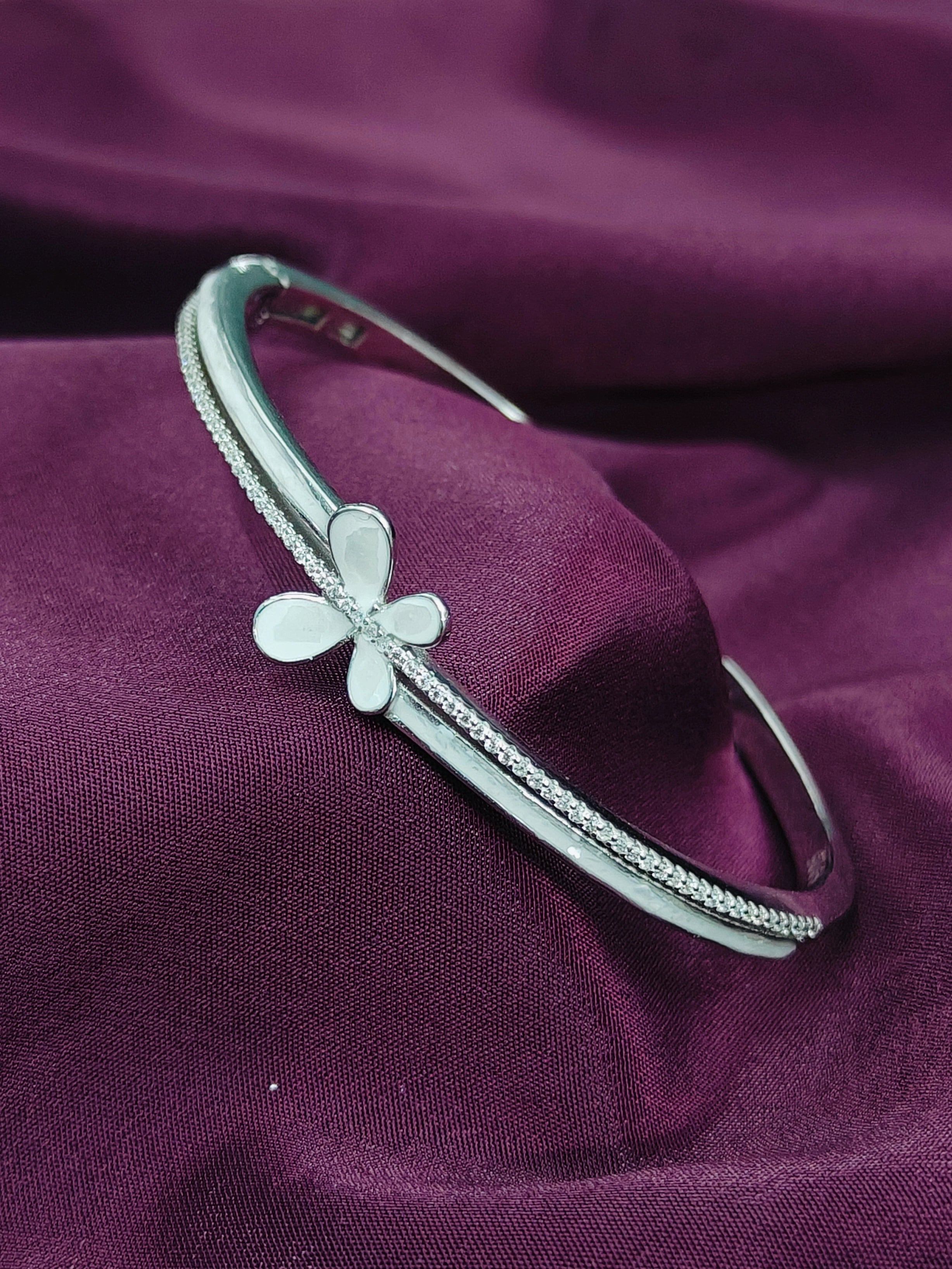 Silver bracelet with a flower charm on a purple fabric background