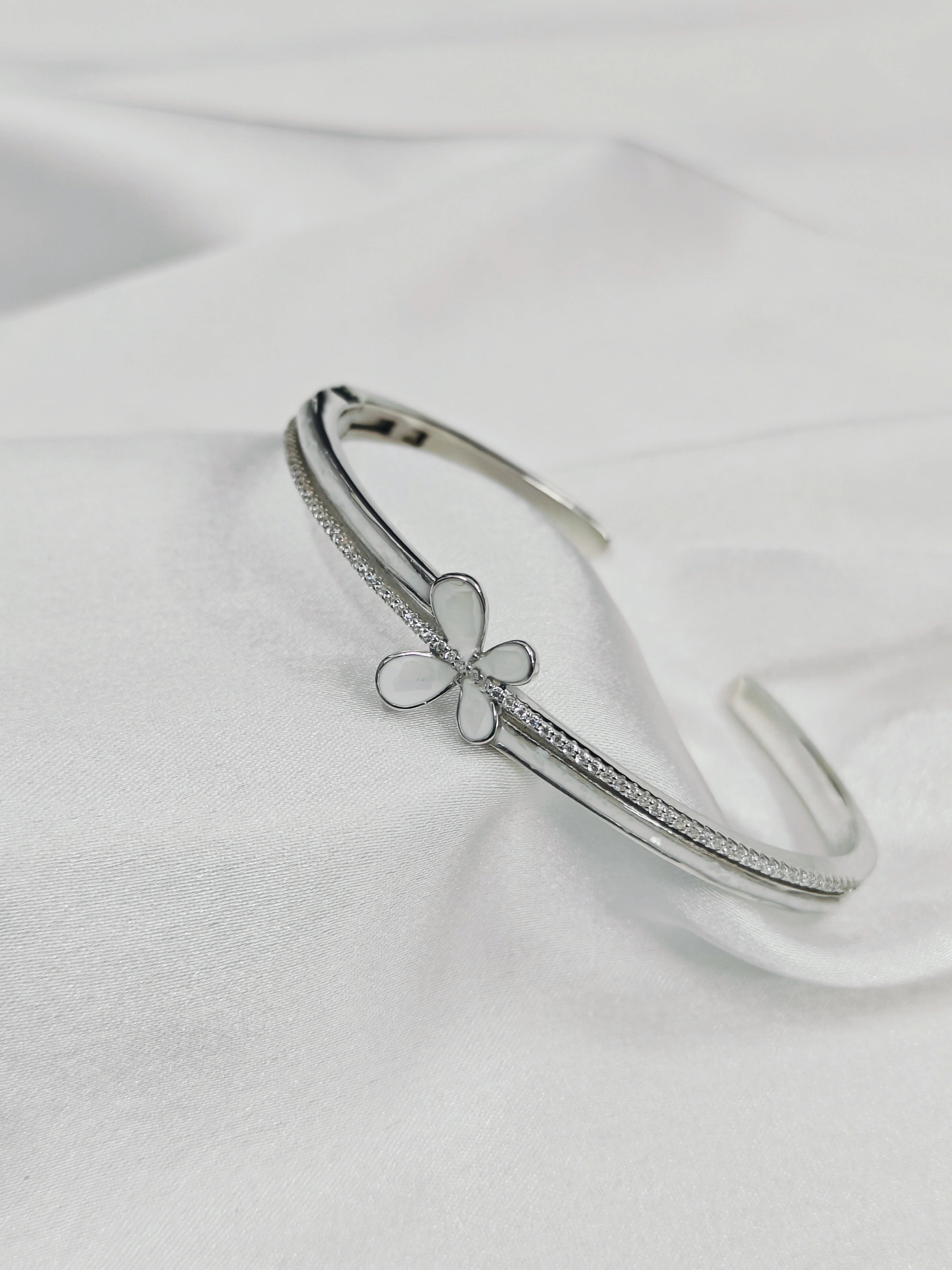 Silver bracelet with a clover charm on a white satin background