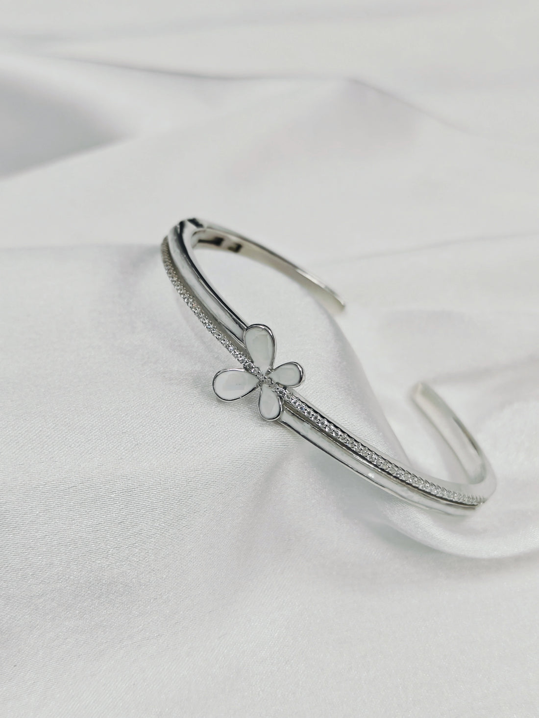 Silver bracelet with a clover charm on a white satin background