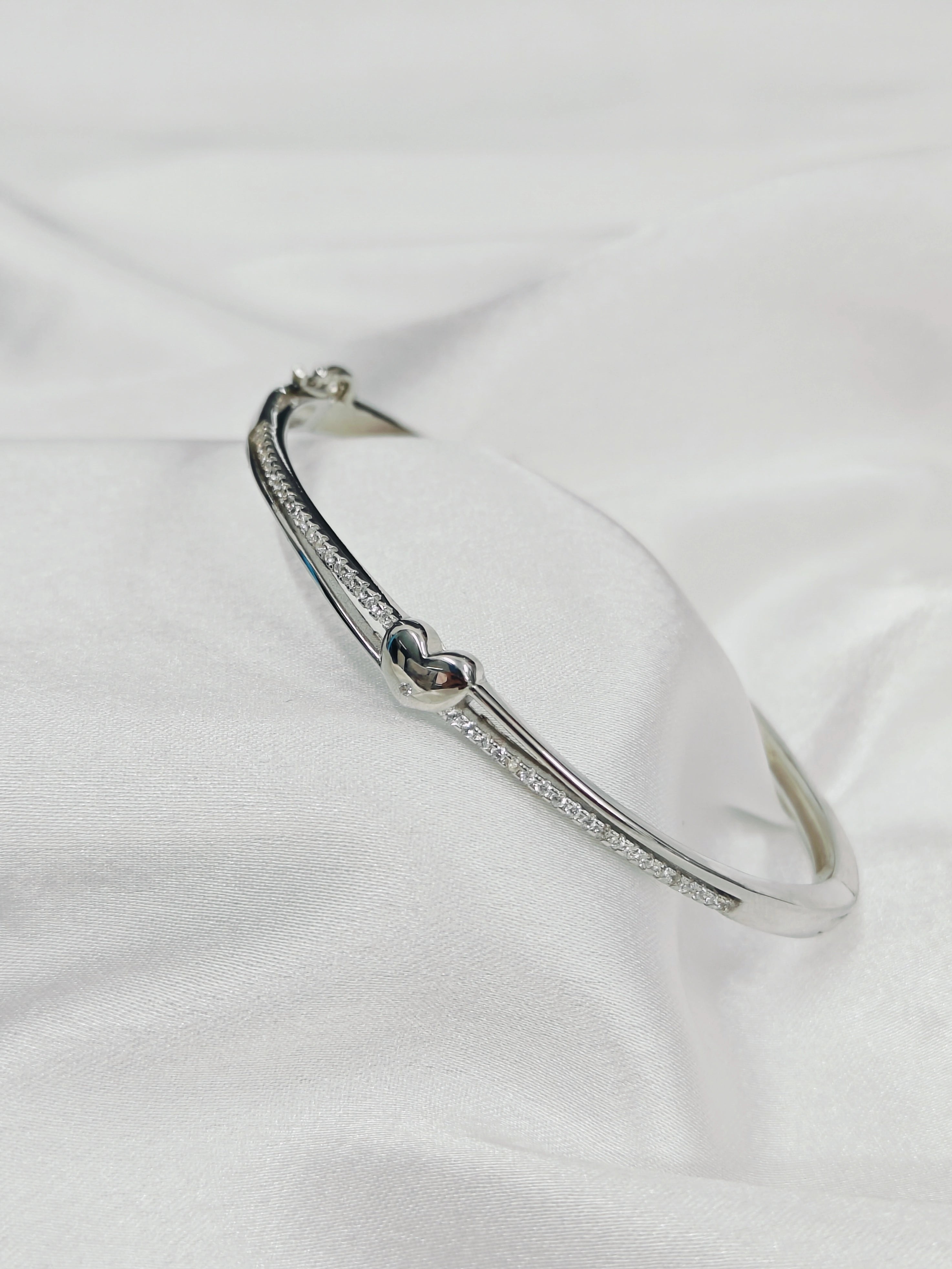 Silver bracelet with heart design on a white fabric background