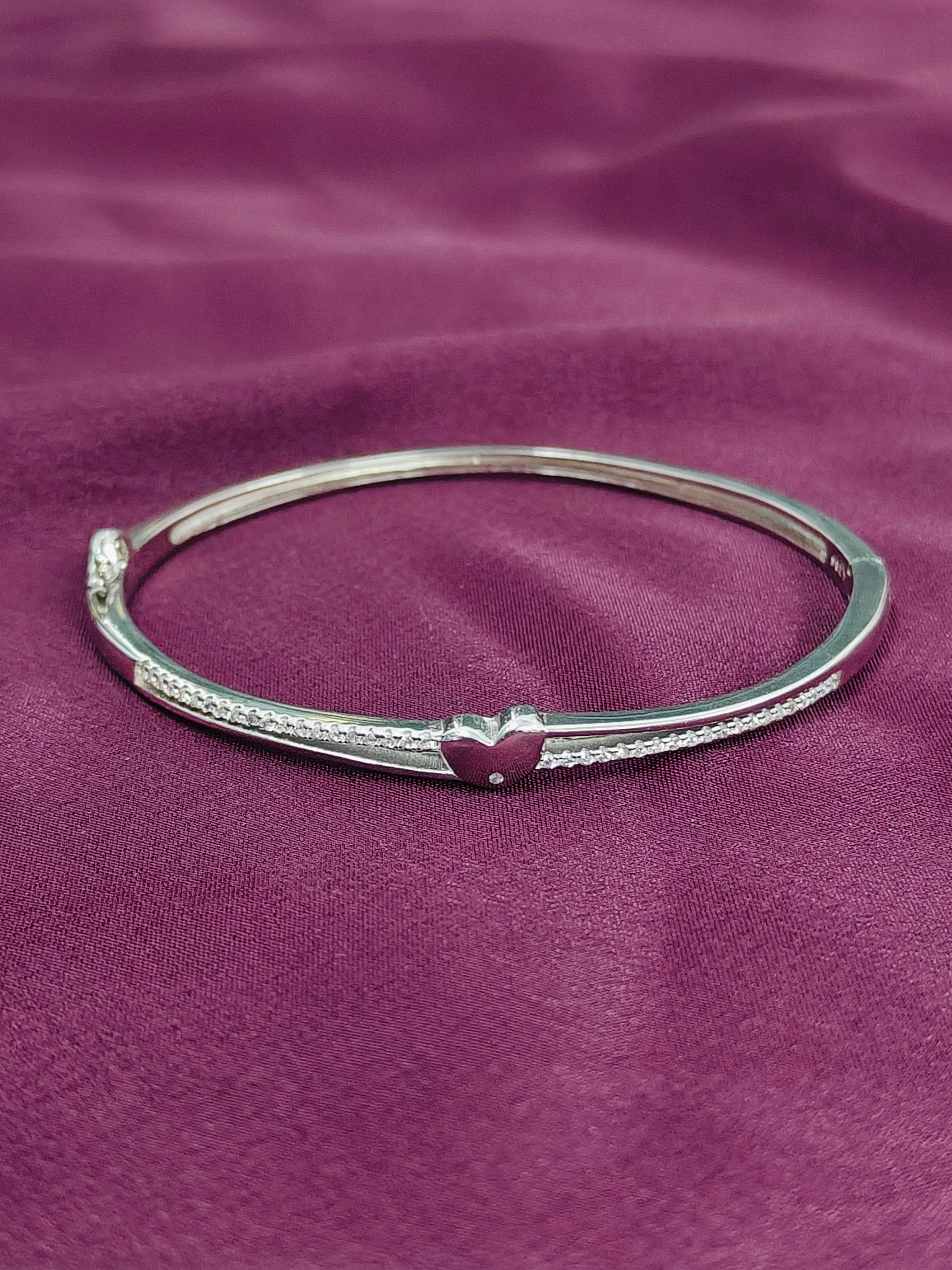Silver bracelet with a heart charm on a purple fabric background