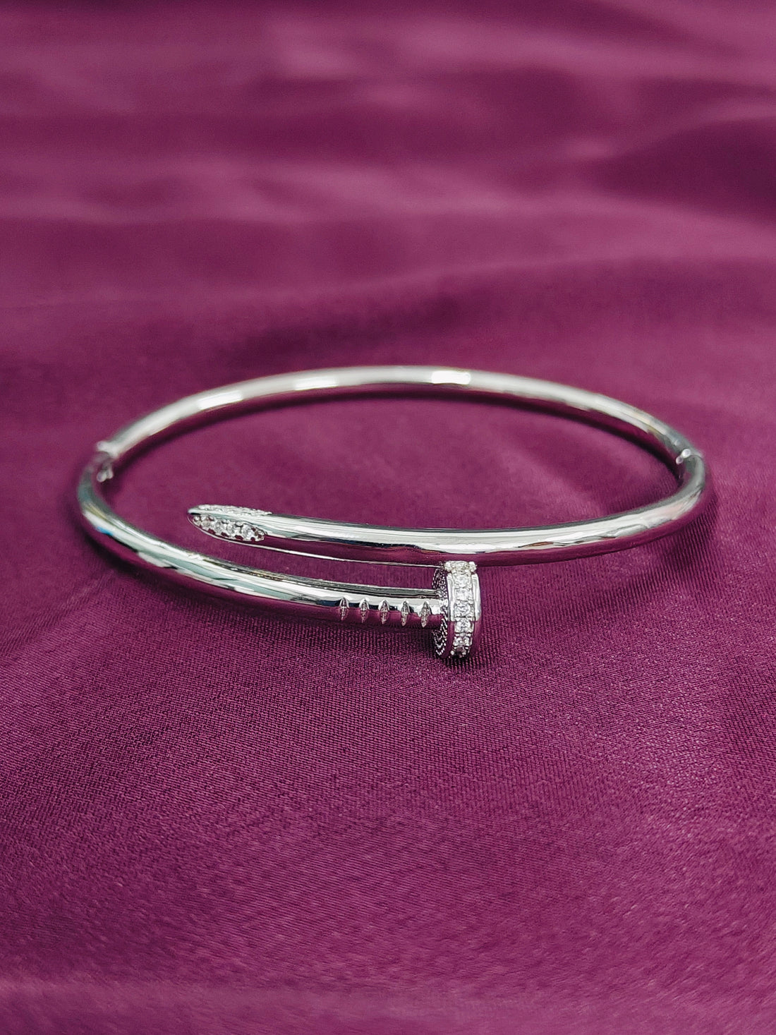 Silver bracelet with a decorative element on a purple fabric background