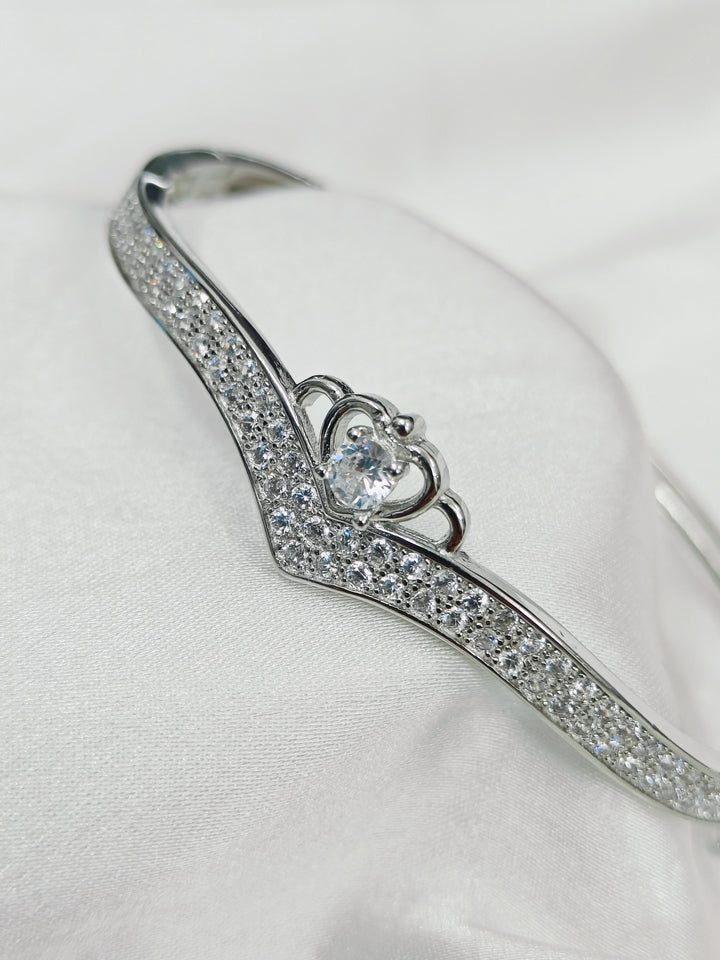 Silver bracelet with heart-shaped clasp and clear stones on a white background