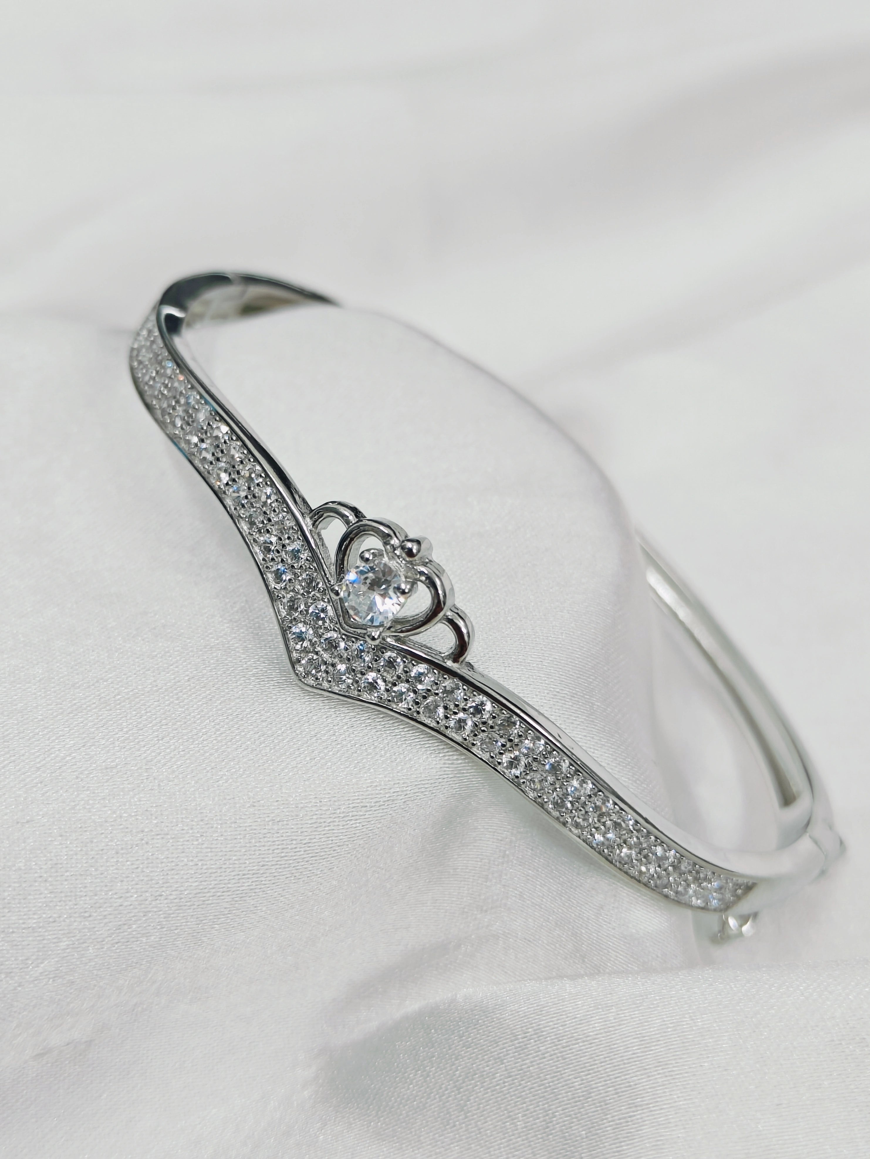 Silver bracelet with heart-shaped center and clear stones on a white background
