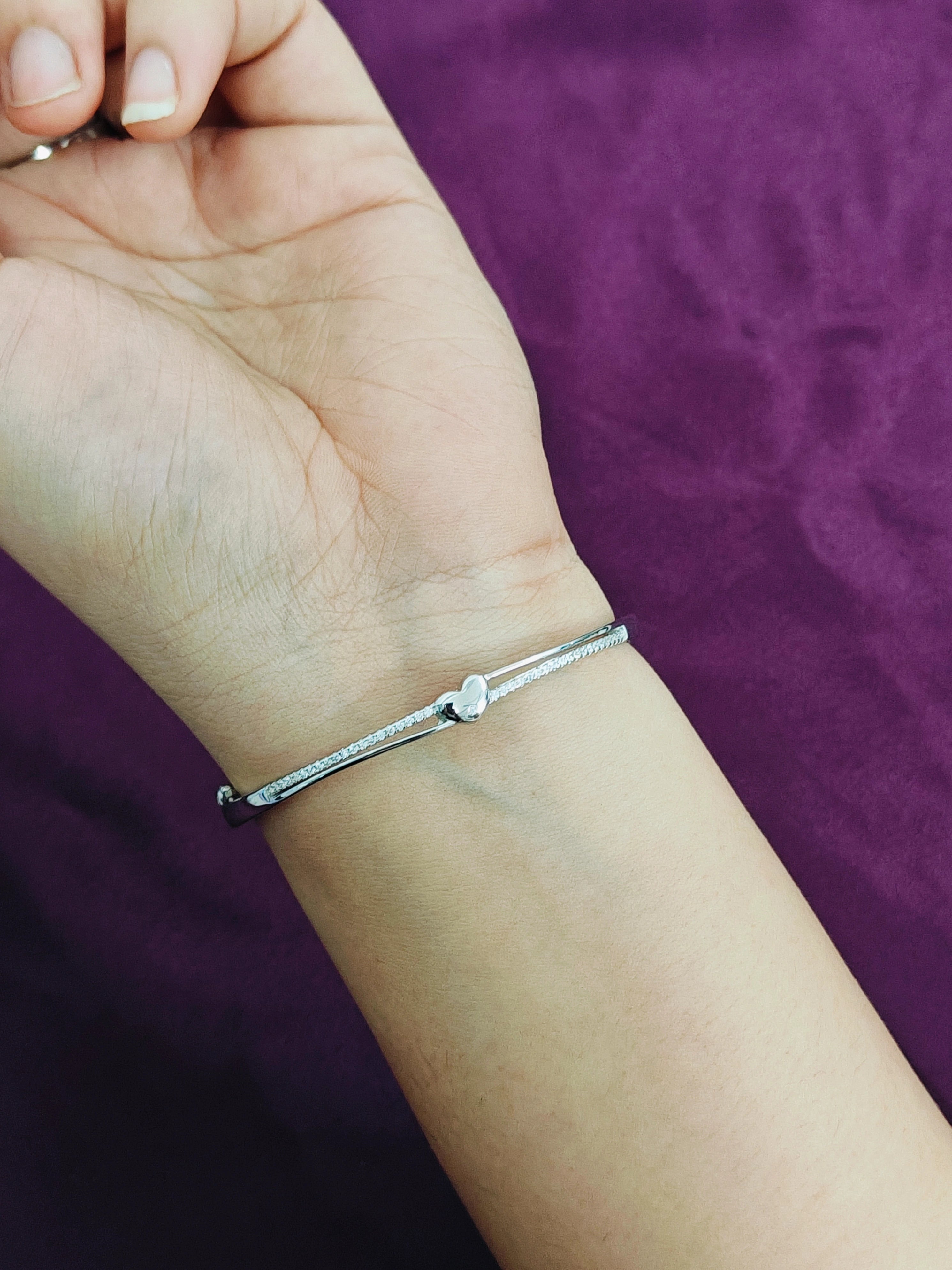 Silver bracelet on a wrist with a purple fabric background