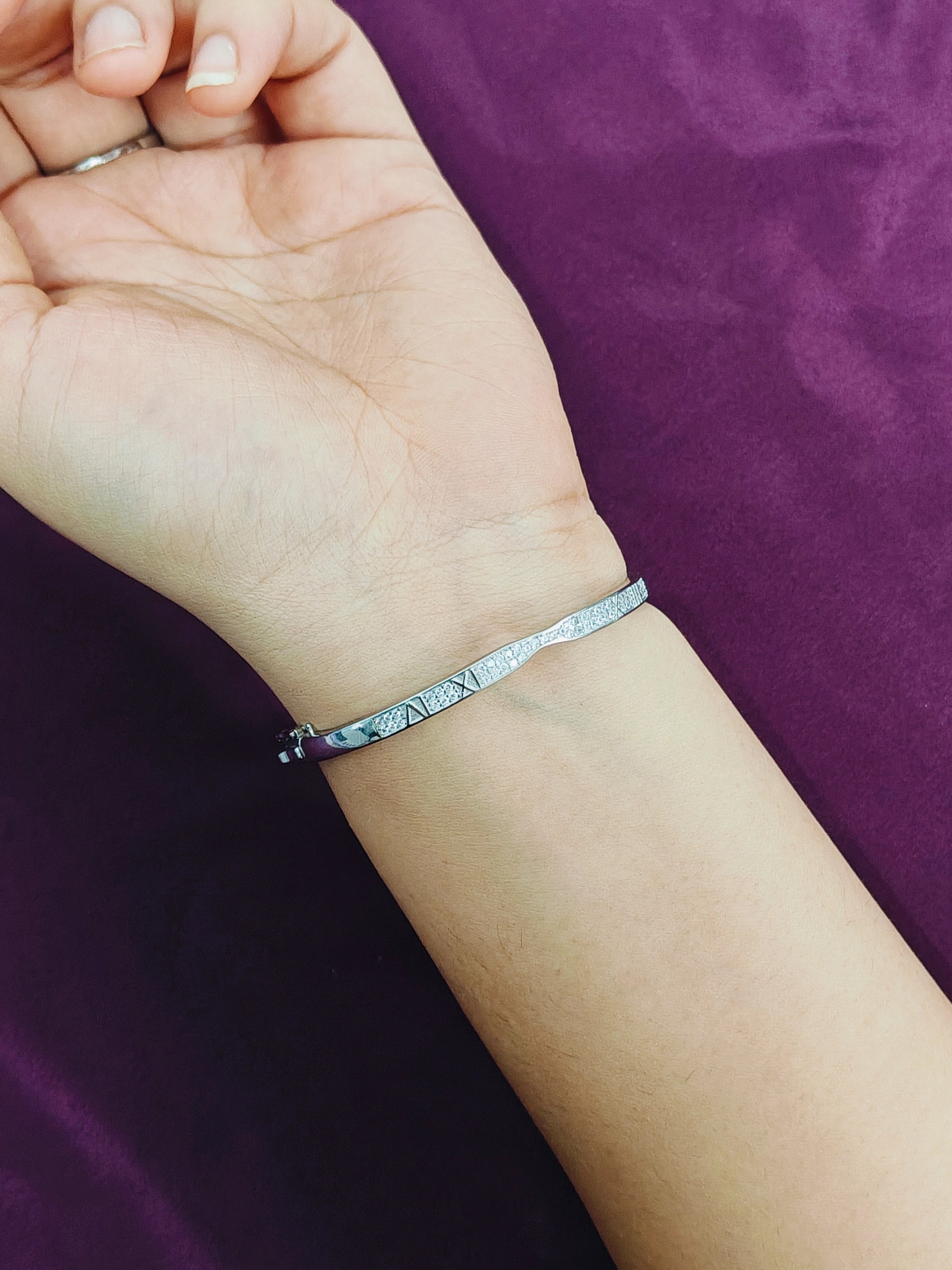 Silver bracelet on a wrist against a purple background