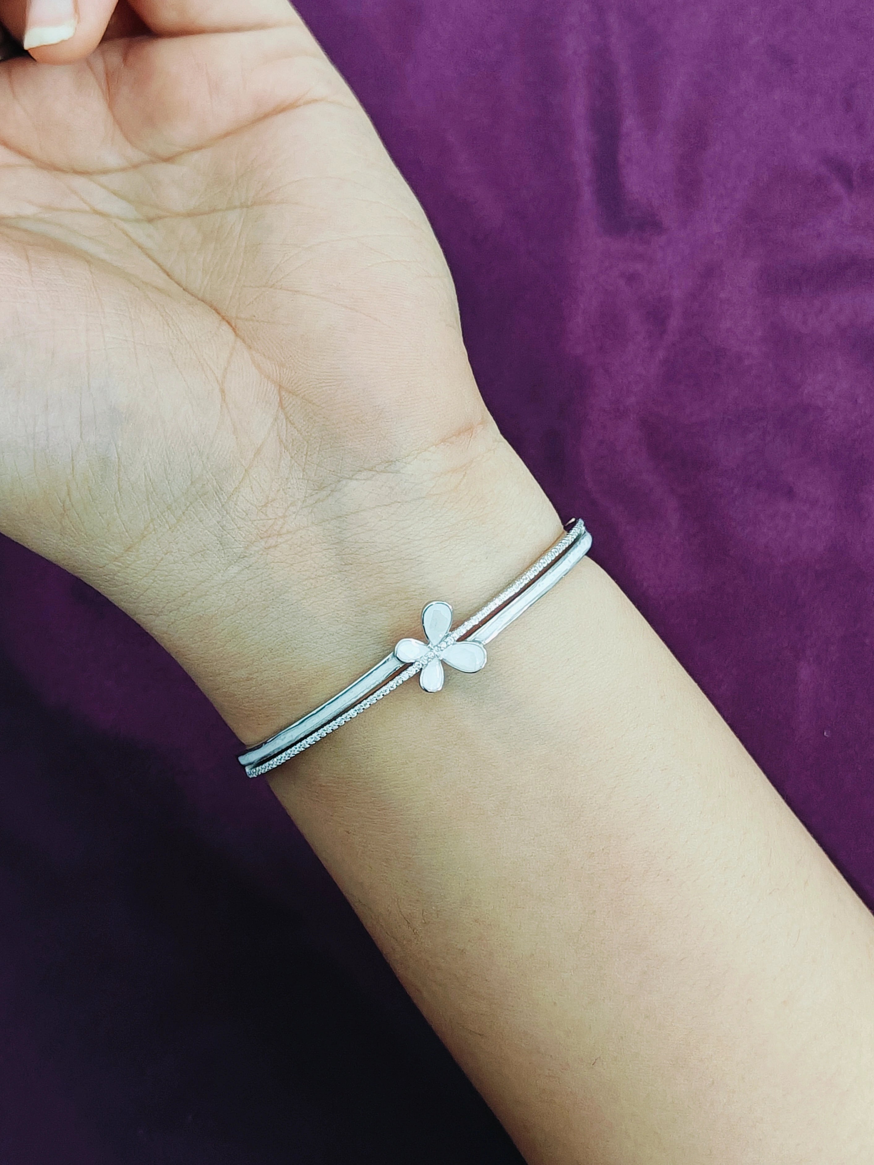 Silver bracelet with a flower charm on a wrist against a purple background