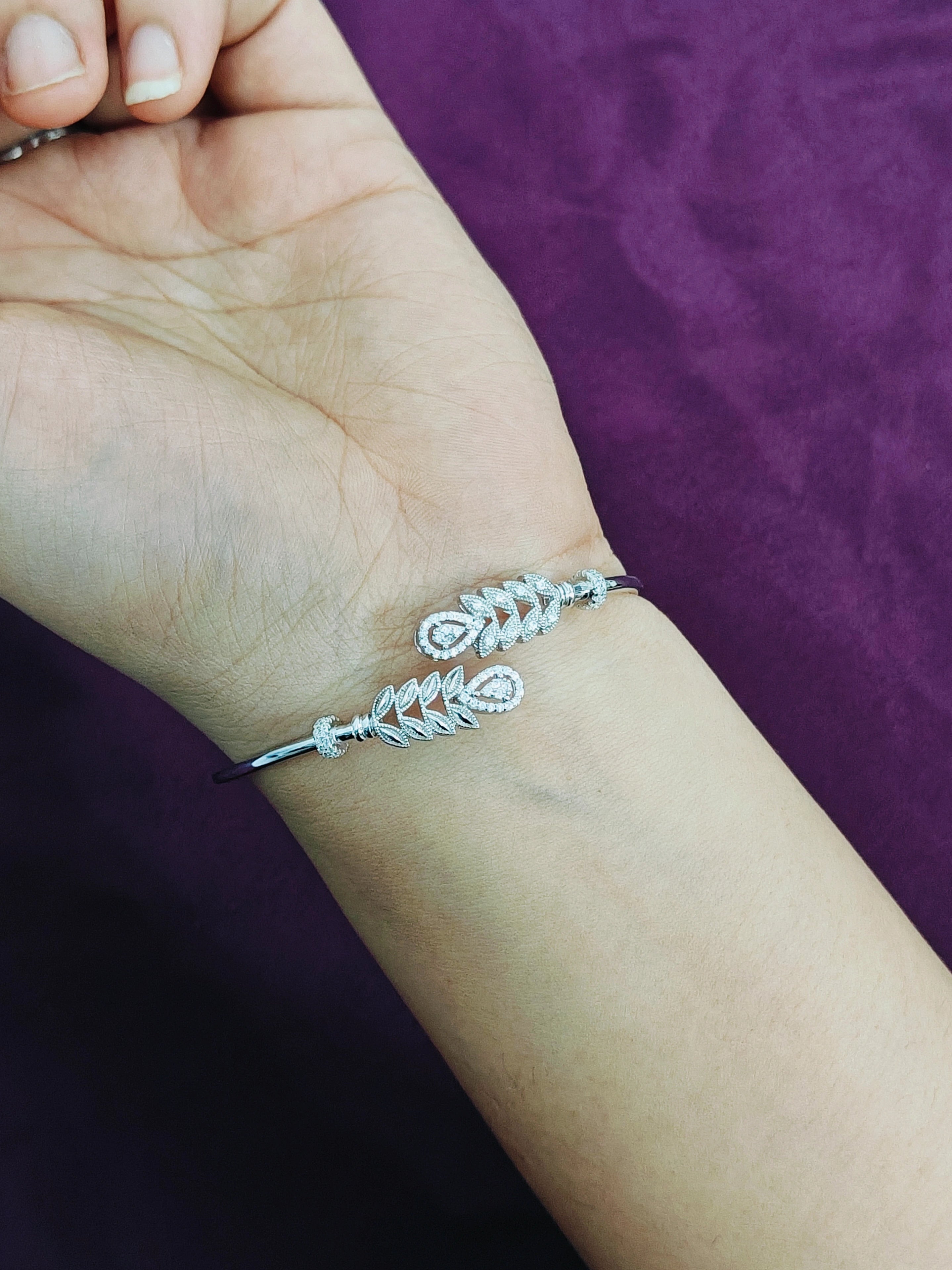 Silver bracelet with leaf design on a wrist against a purple background