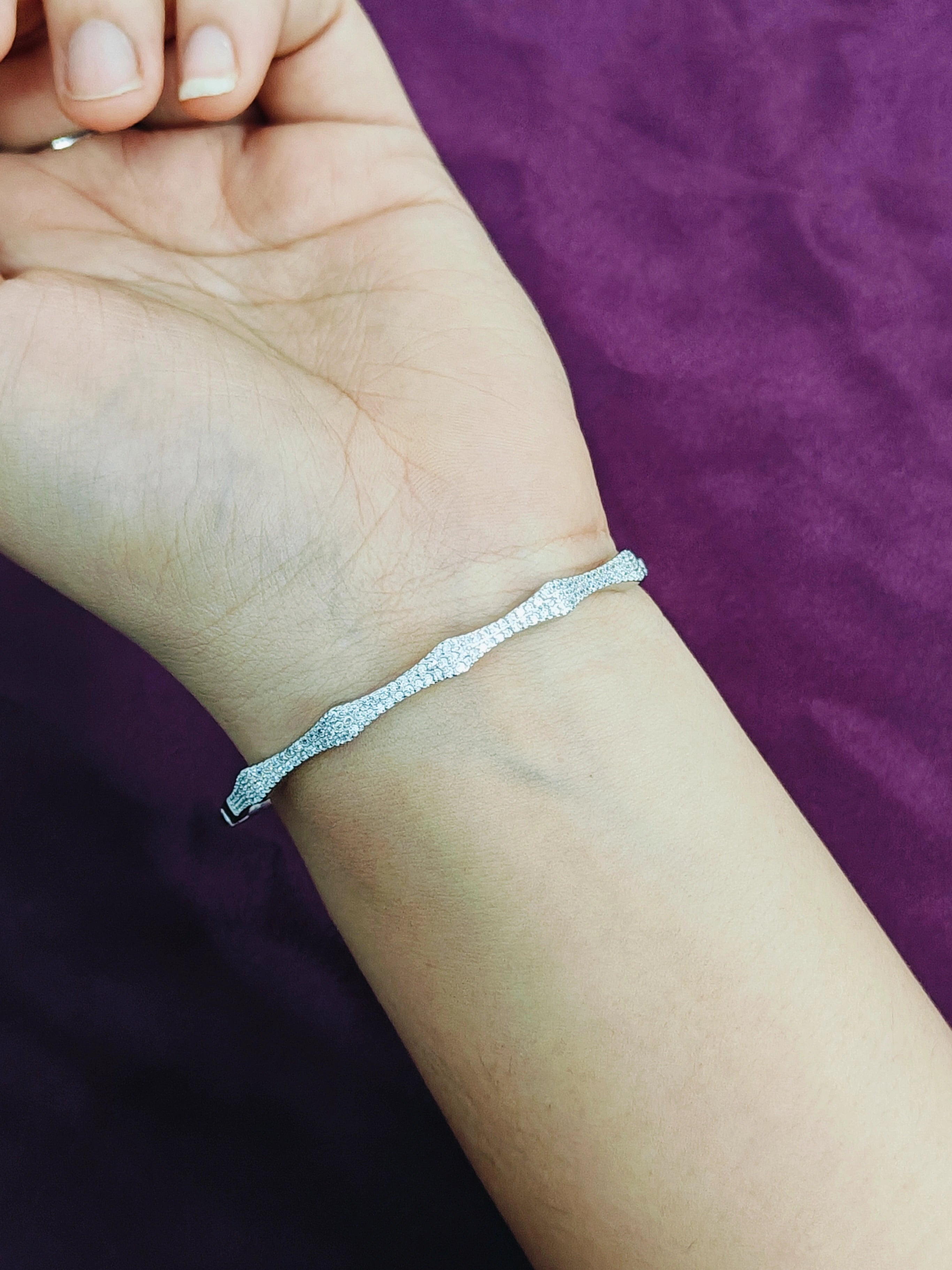 Silver bracelet on a wrist with a purple background