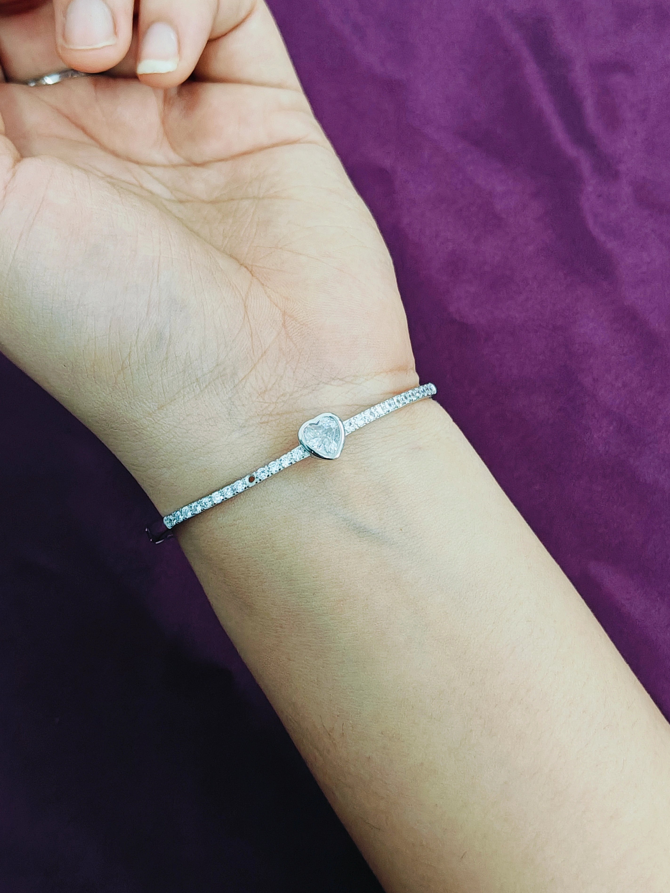Silver bracelet with a heart-shaped charm on a wrist against a purple background