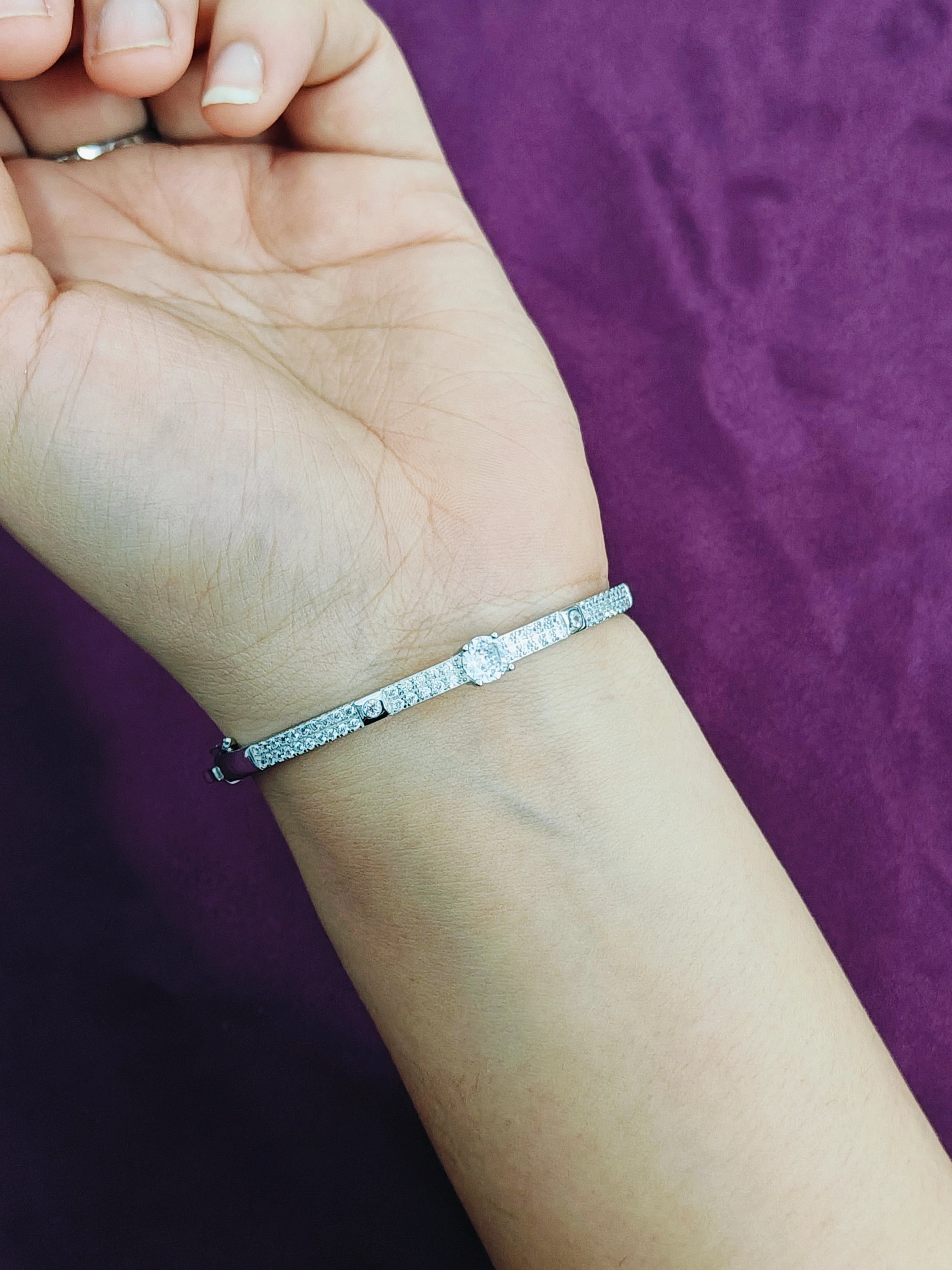 Silver bracelet on a wrist with a purple background