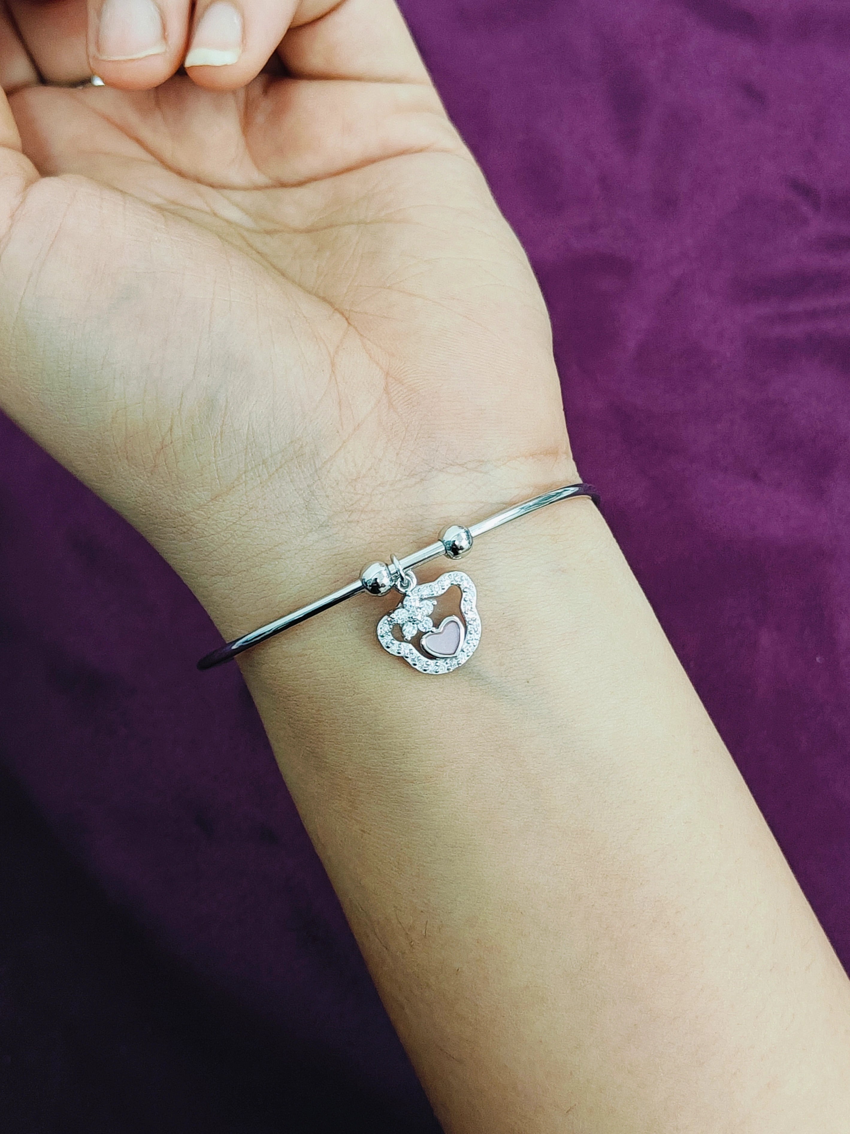 Silver bracelet with a heart-shaped charm on a wrist against a purple background