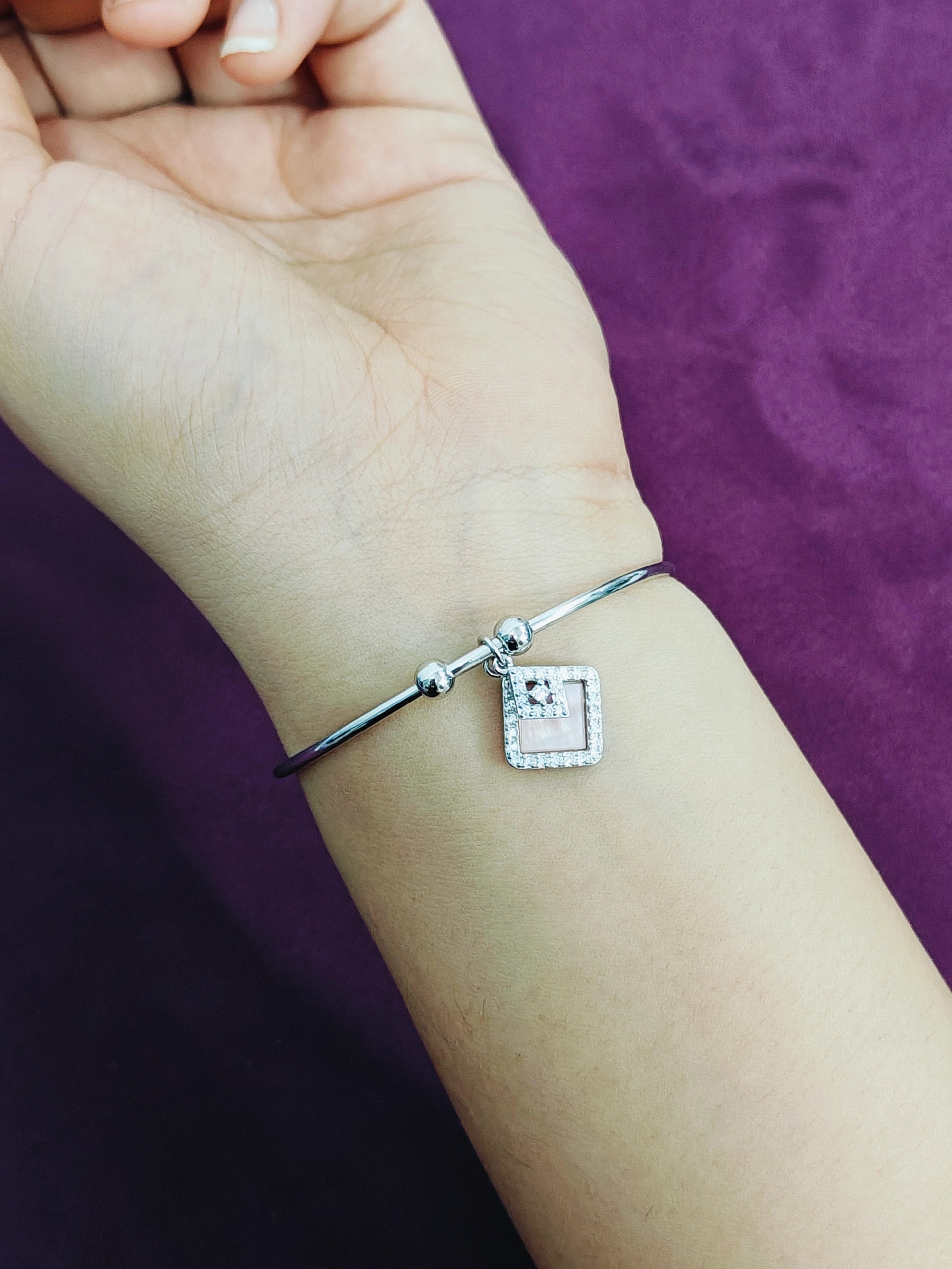 Silver bracelet with a square charm on a wrist against a purple background