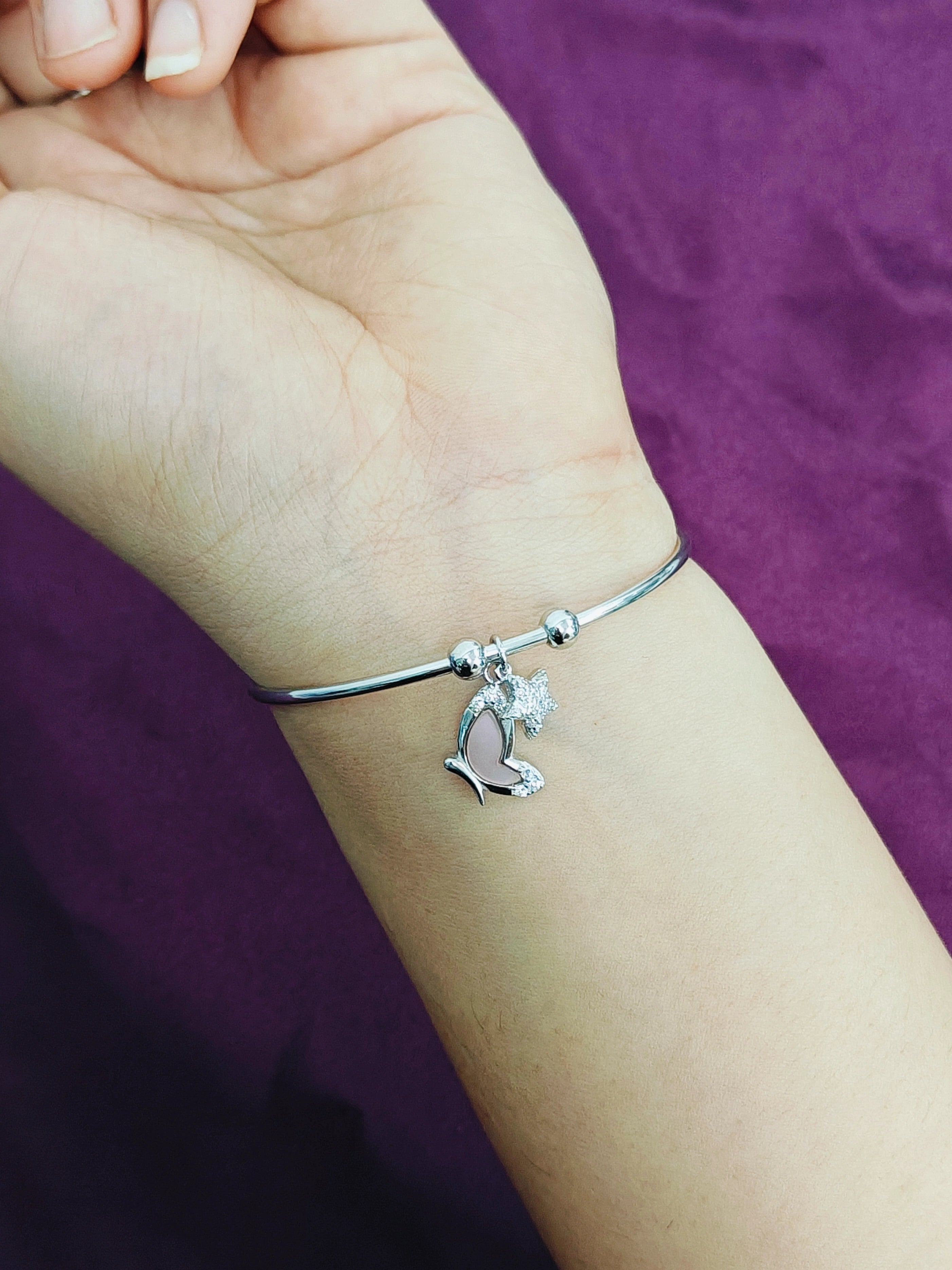 Silver bracelet with a dove charm on a wrist against a purple background